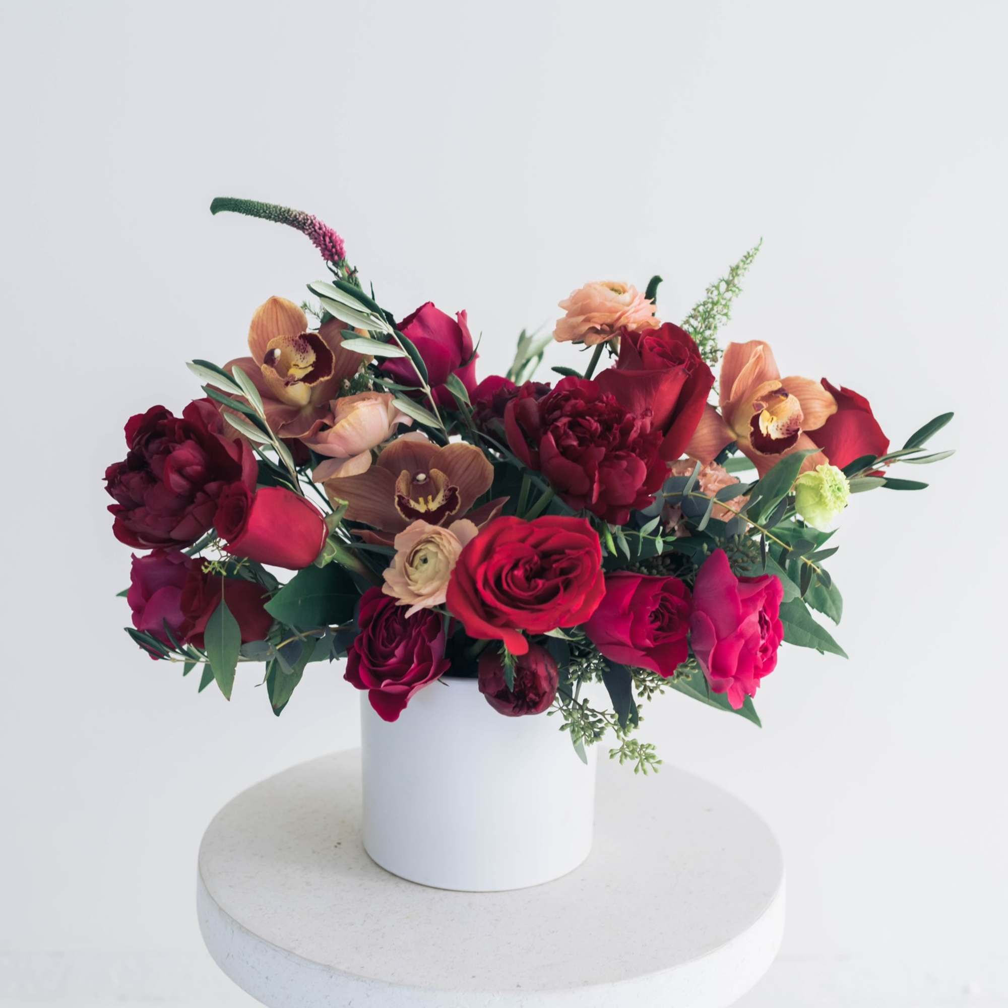 Mixed bouquet of red and peach flowers in a white vase