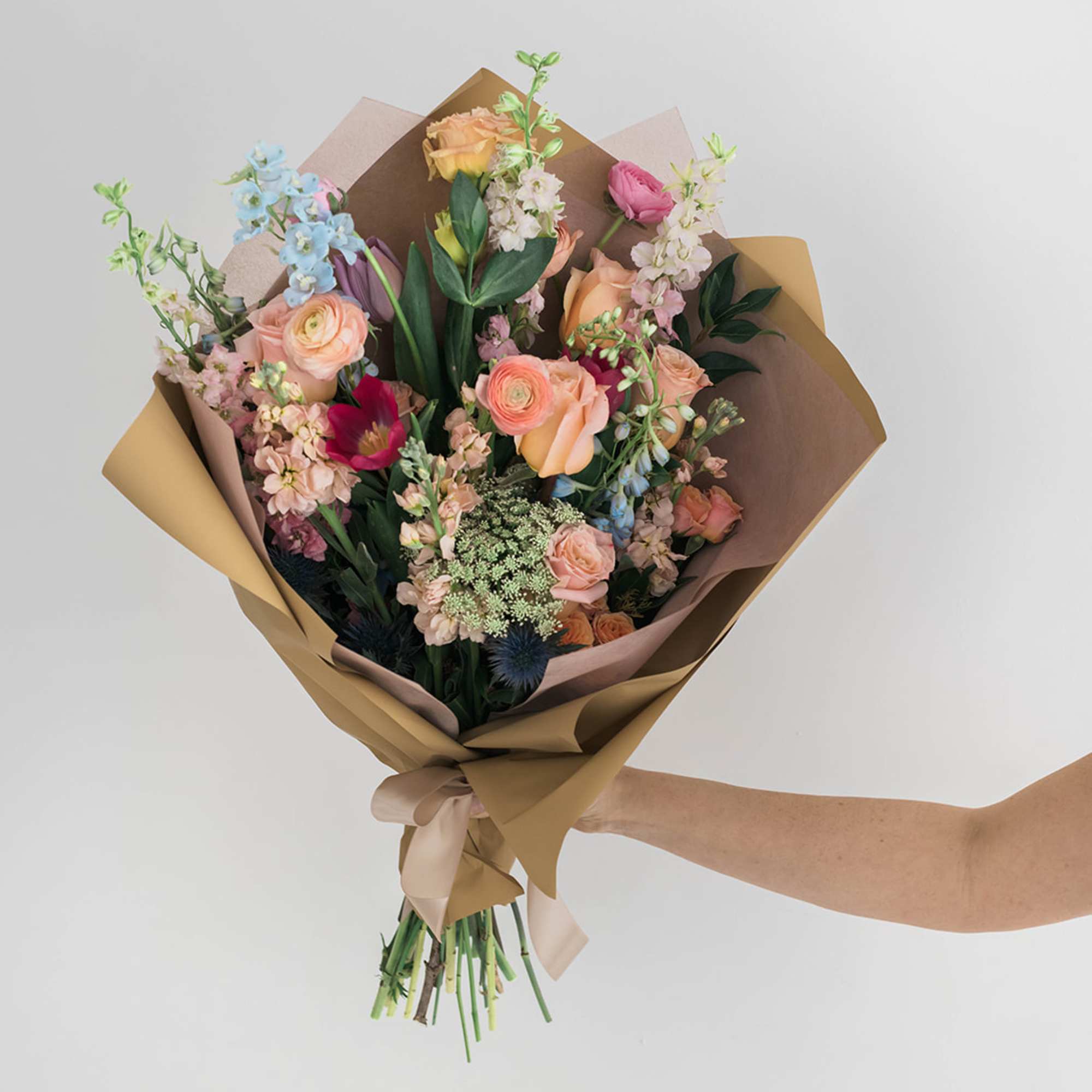 Hand-tied bouquet of pastel mixed flowers wrapped in brown paper