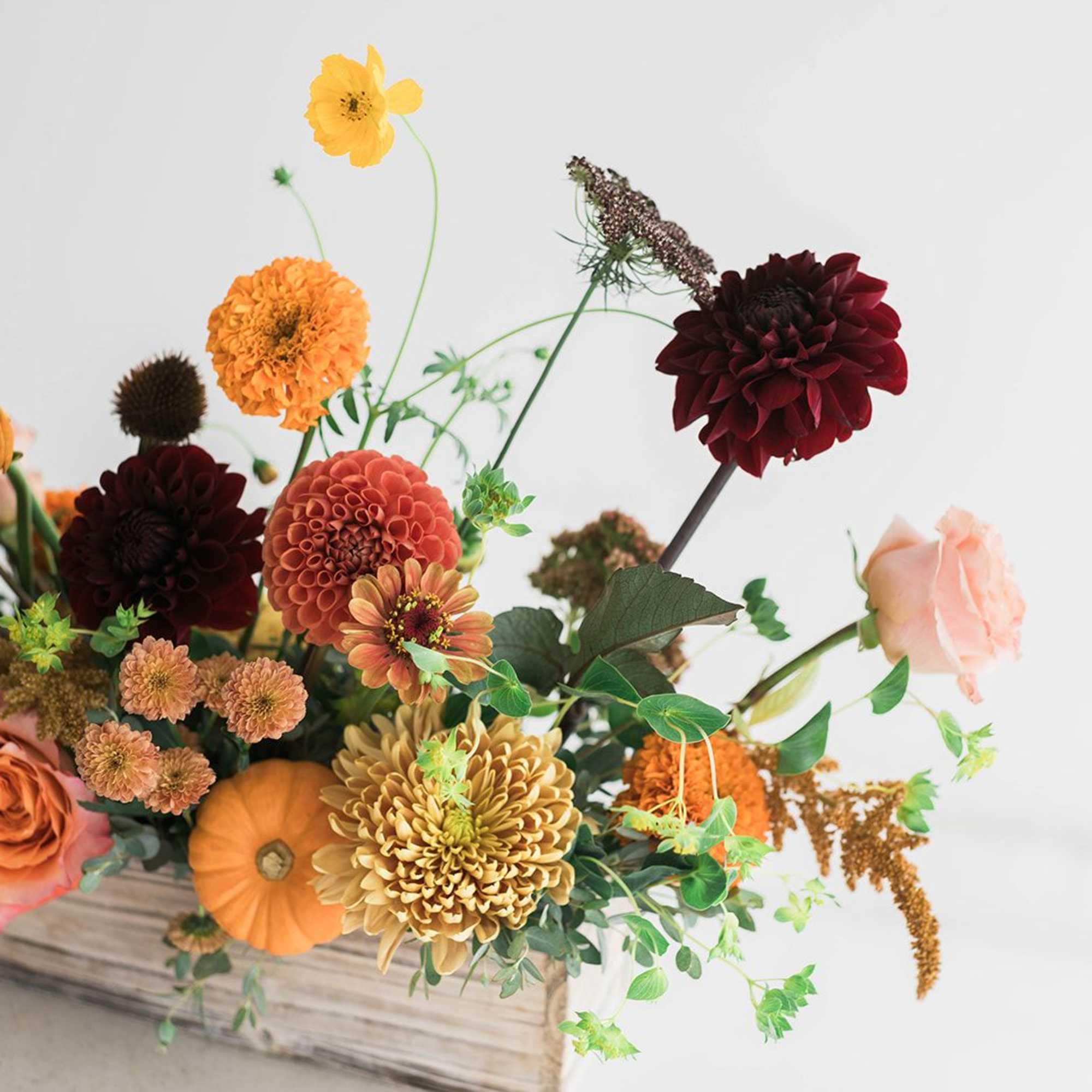 Autumn floral arrangement with dahlias, roses, and orange blooms in a wooden box