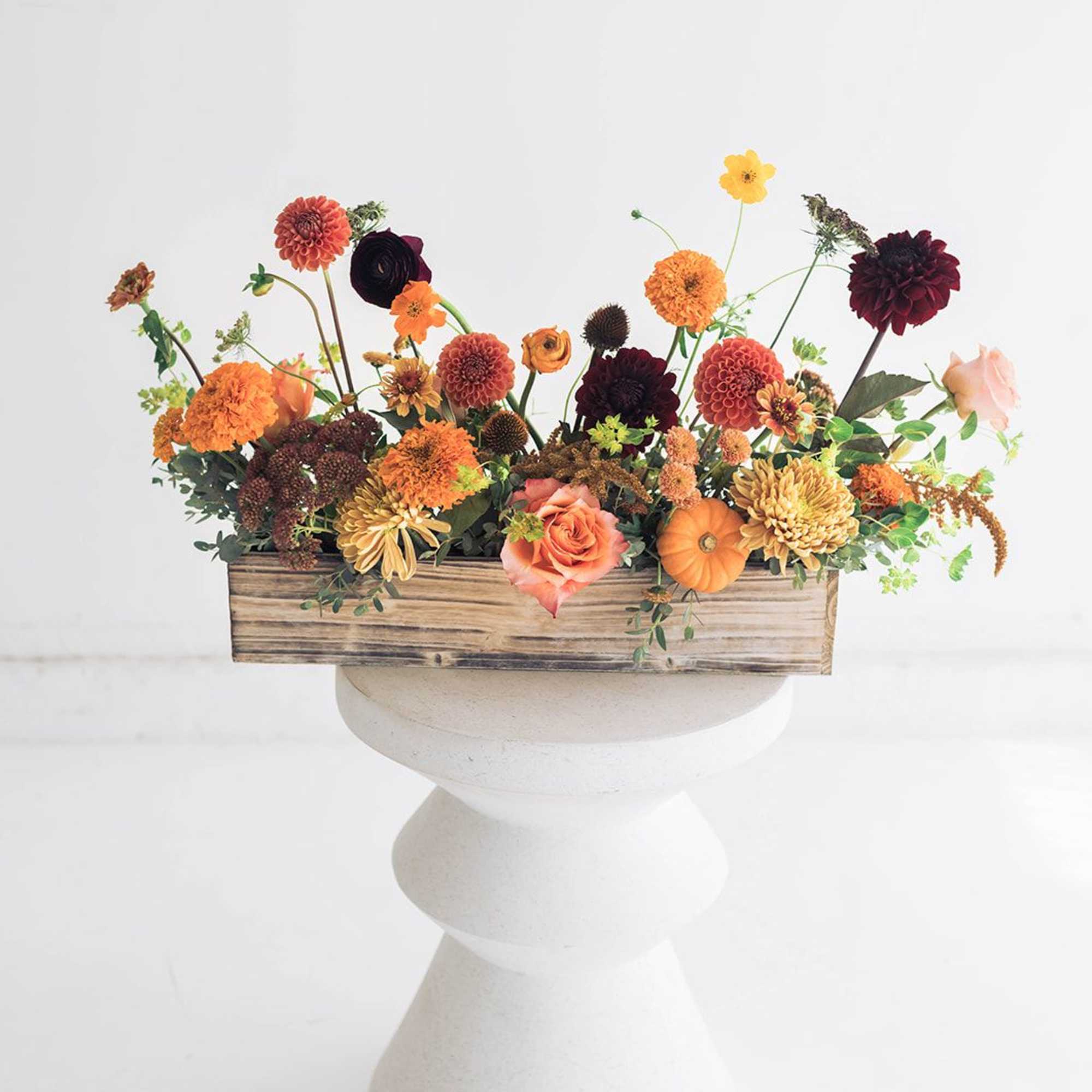 Mixed orange and burgundy flowers in a wooden box on a pedestal