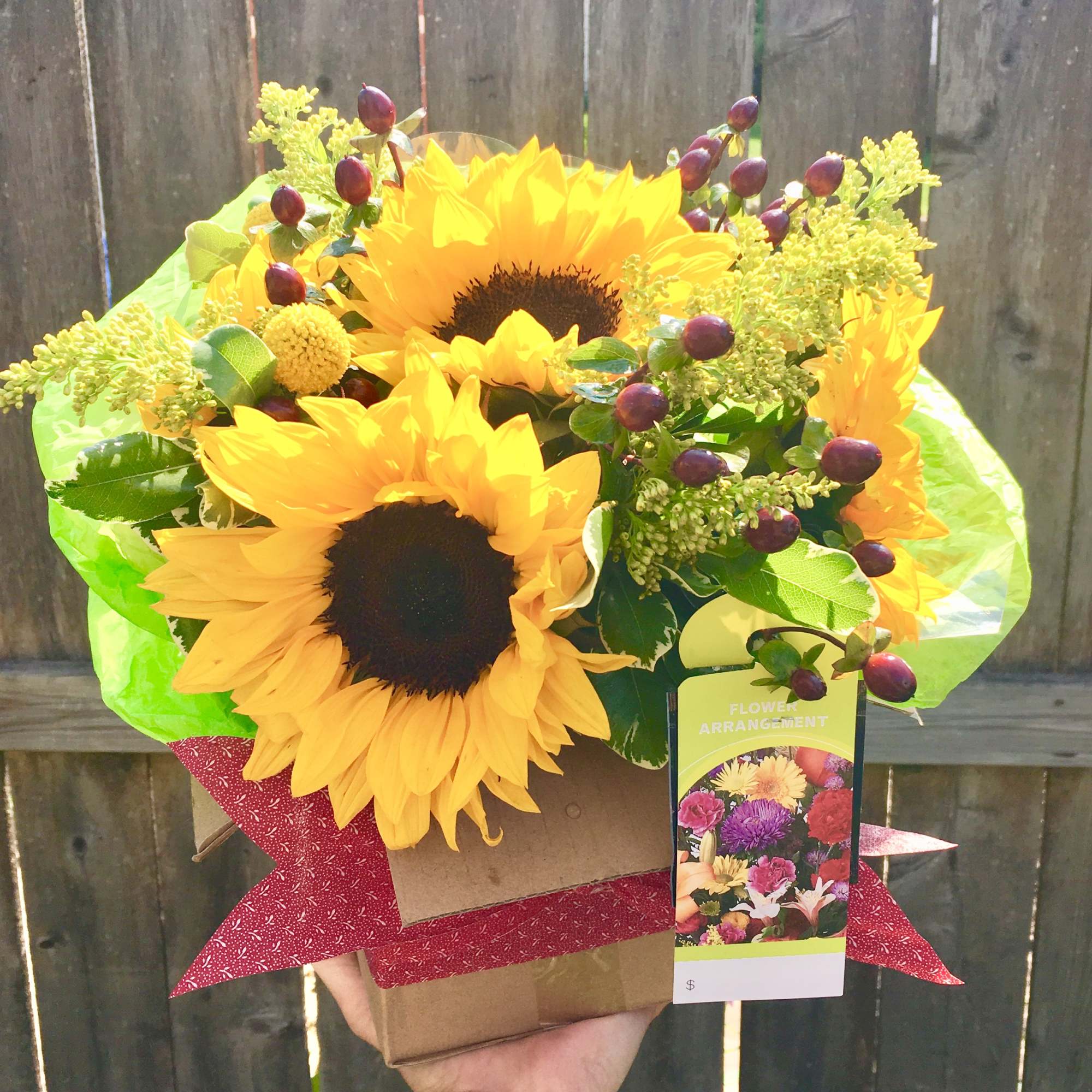 Bright yellow sunflower arrangement with red berries in a kraft box with red bow