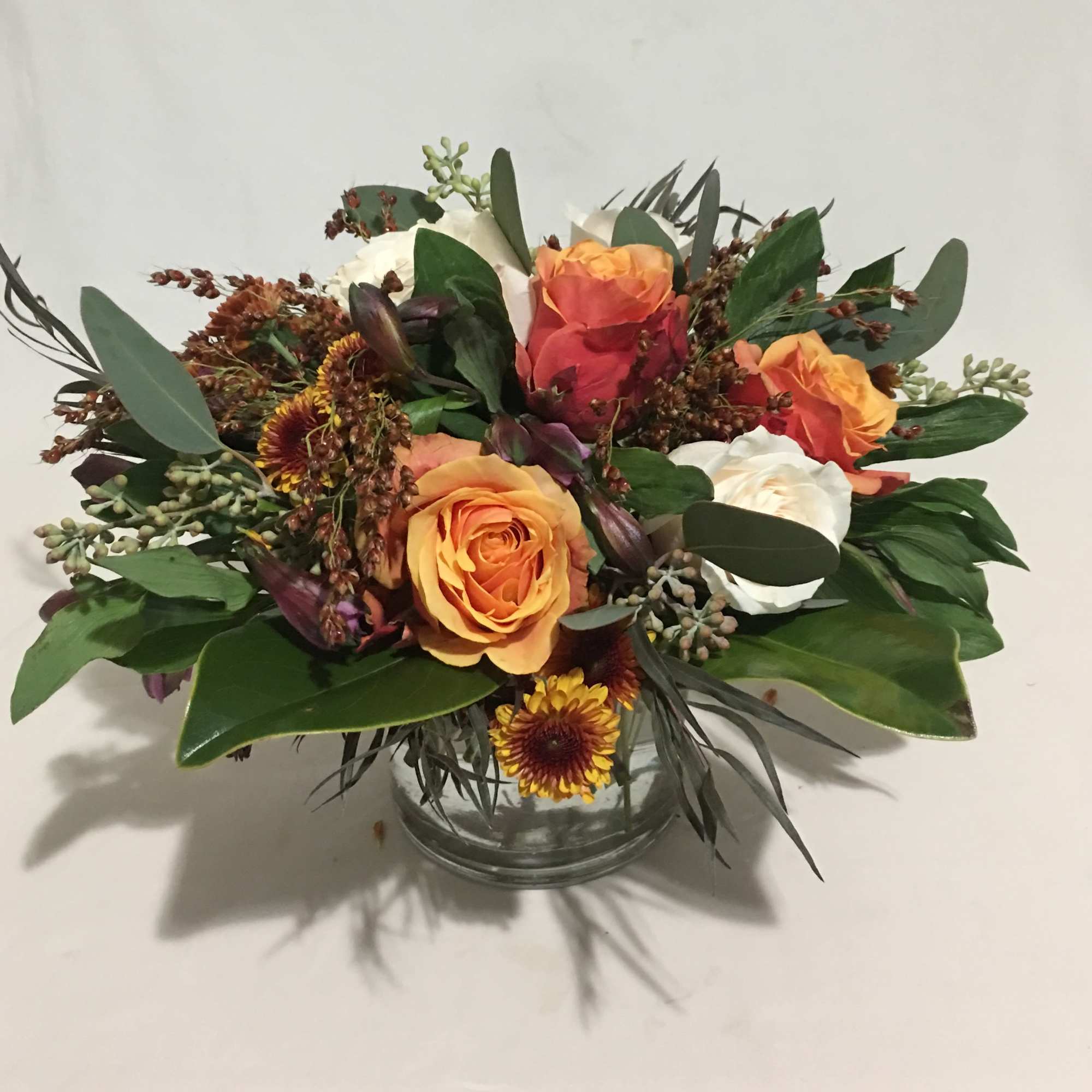 Low arrangement of orange and white roses with yellow mums in a clear glass vase