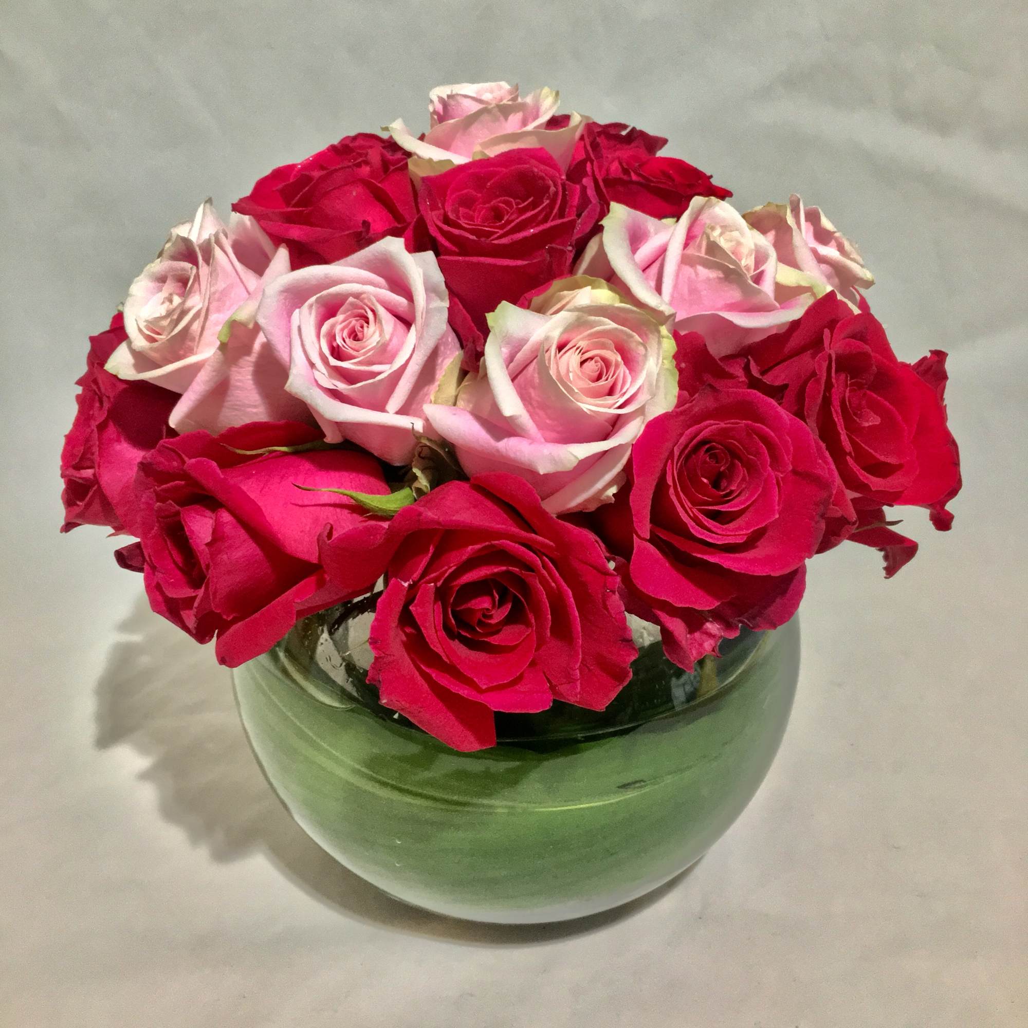 Compact arrangement of hot pink and light pink roses in a round green glass vase