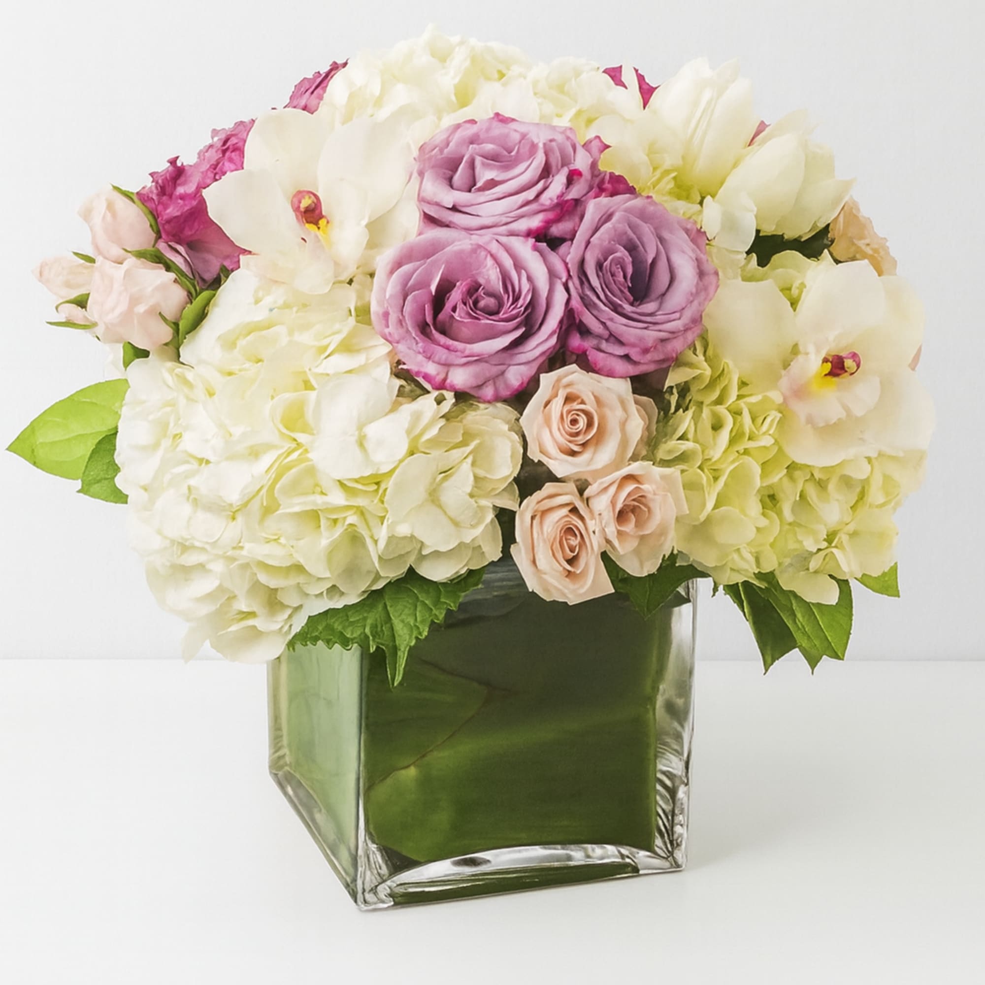 Mixed pink, white, and lavender flowers arranged in a square glass vase