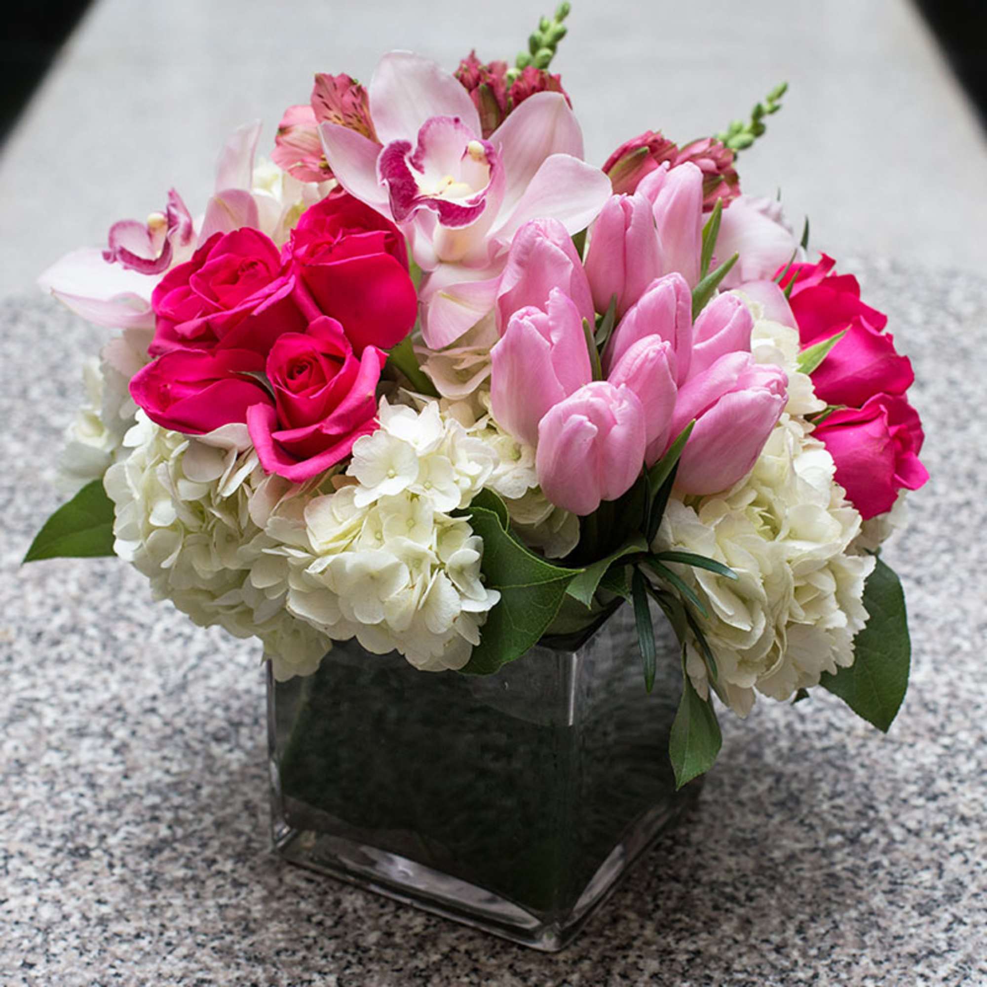 Pink roses and tulips arranged with white hydrangeas in a square glass vase