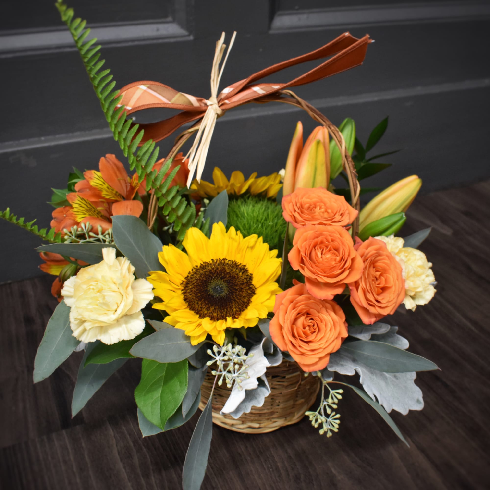 Basket arrangement with sunflowers, orange roses, carnations, and lilies