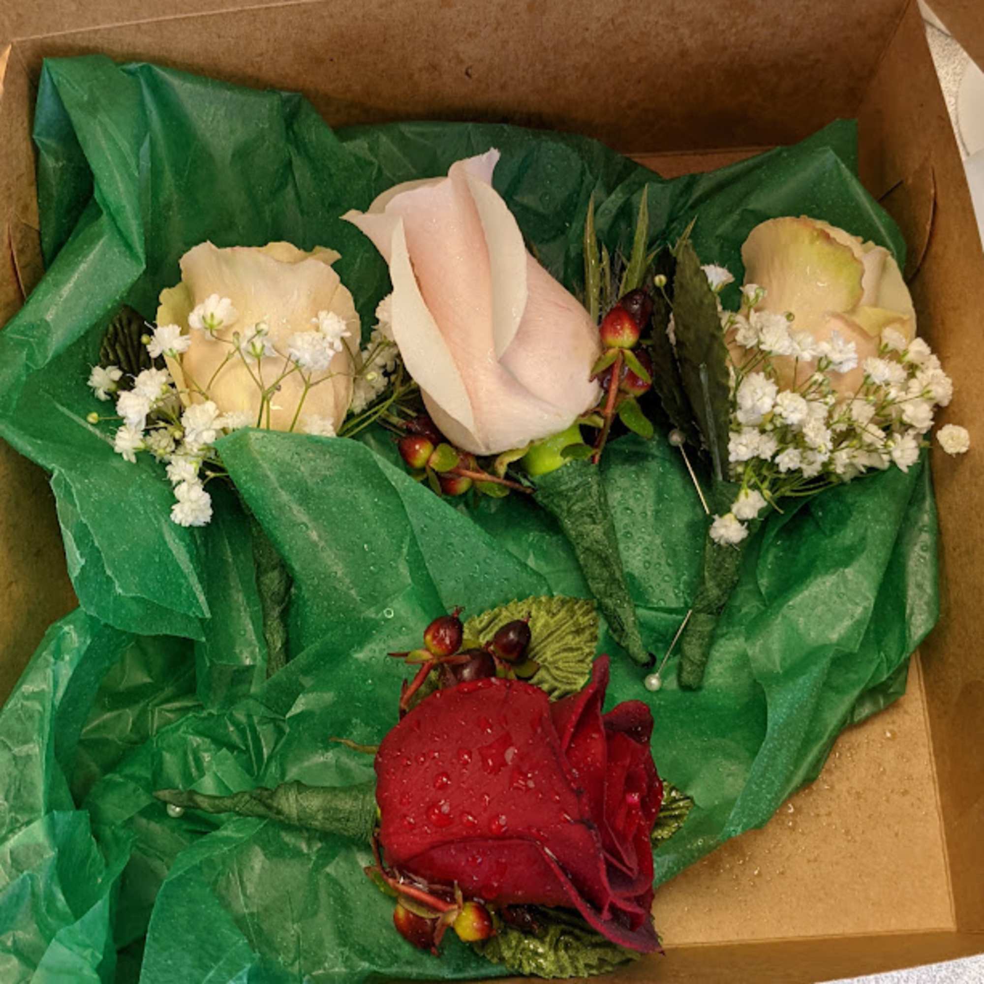 Boxed rose boutonnieres in red, blush, and cream with baby's breath