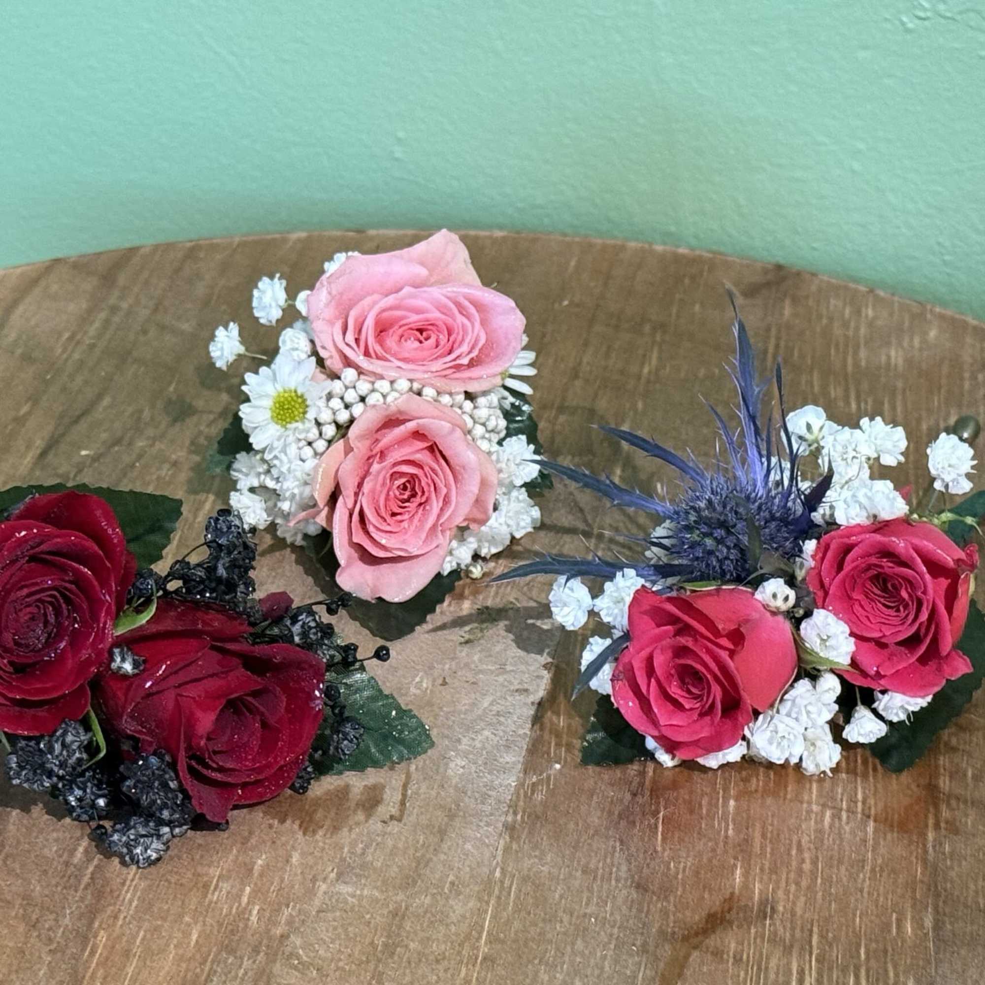 Three small rose corsages with baby's breath on a wooden surface