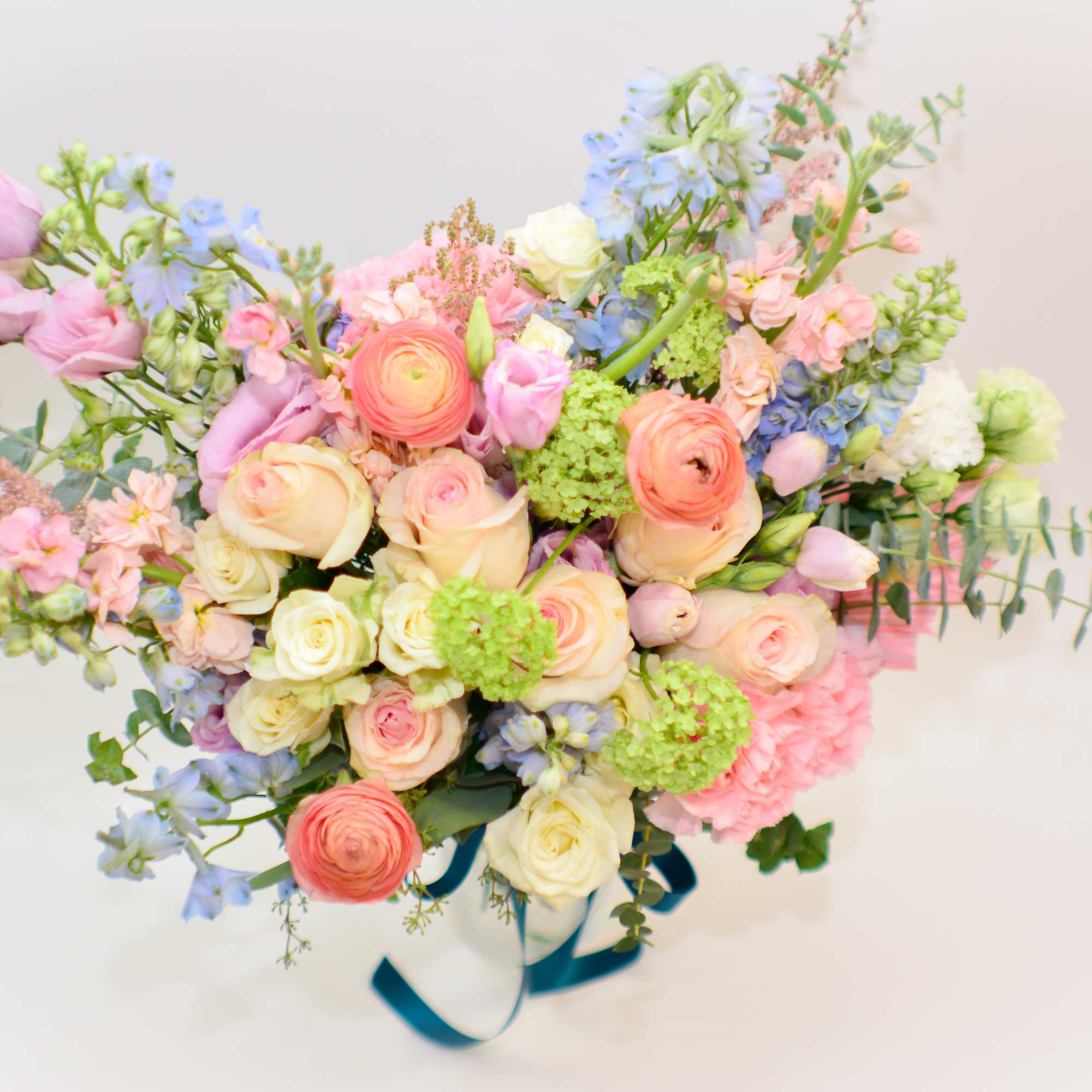 Pastel bouquet of roses, ranunculus, and blue flowers tied with ribbon