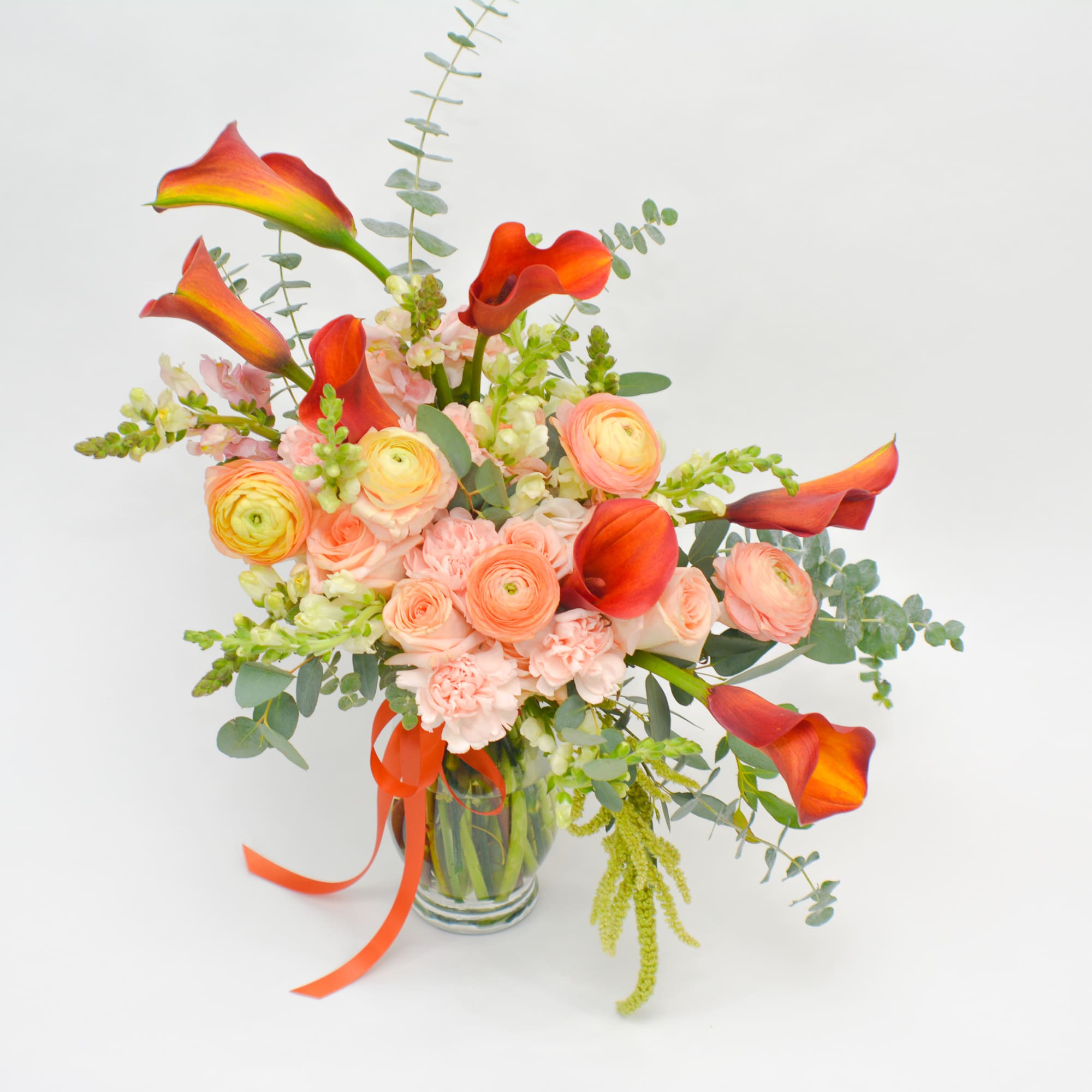 Bouquet of orange calla lilies and peach flowers in a glass vase