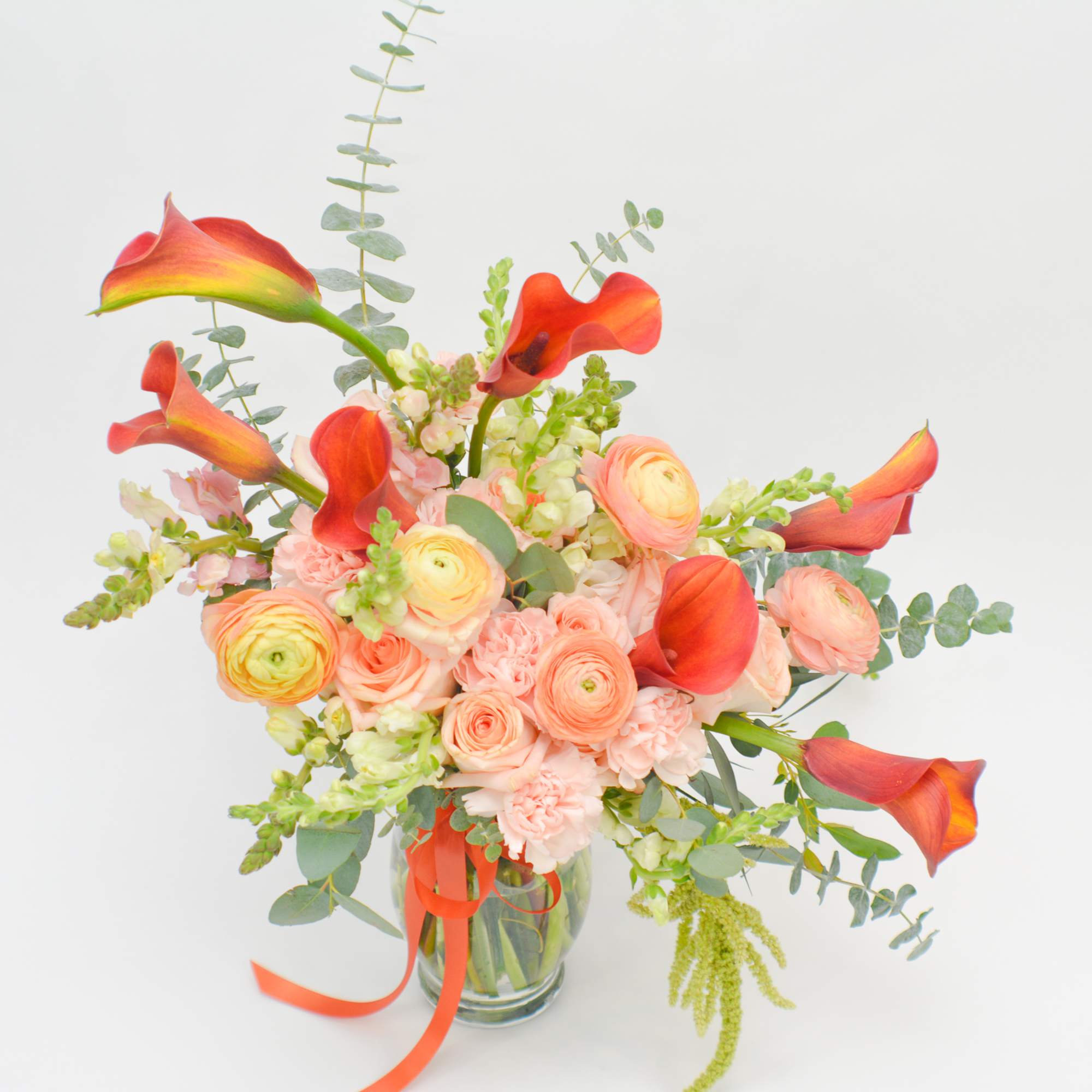 Bouquet of coral calla lilies and peach ranunculus in a glass vase