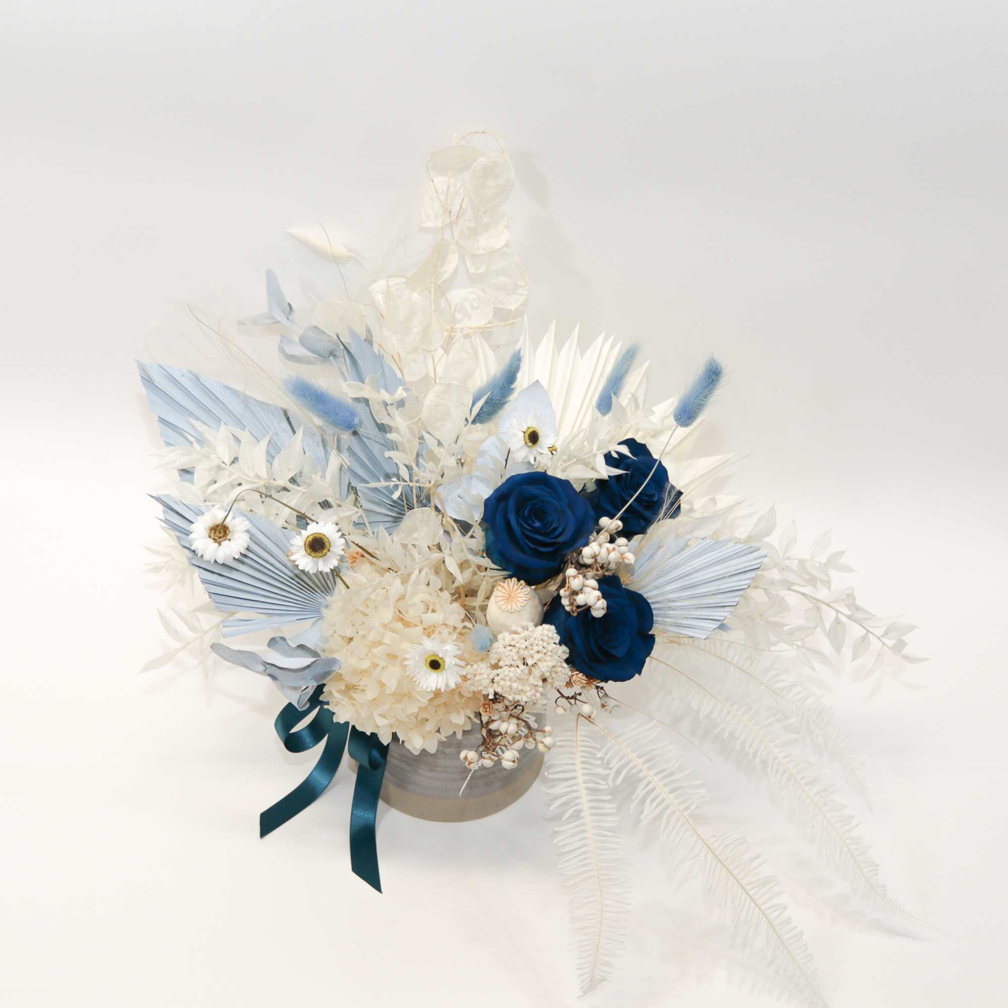 Blue and white floral arrangement in a round container with ribbon