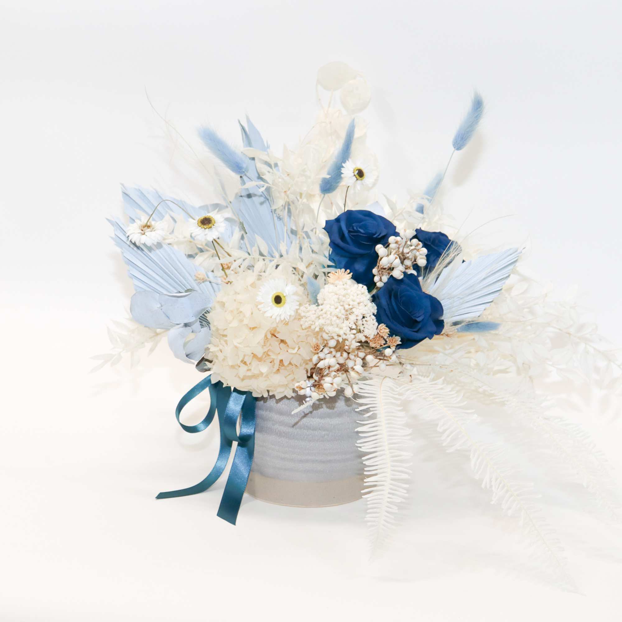 Blue and white floral arrangement in a round box with ribbon