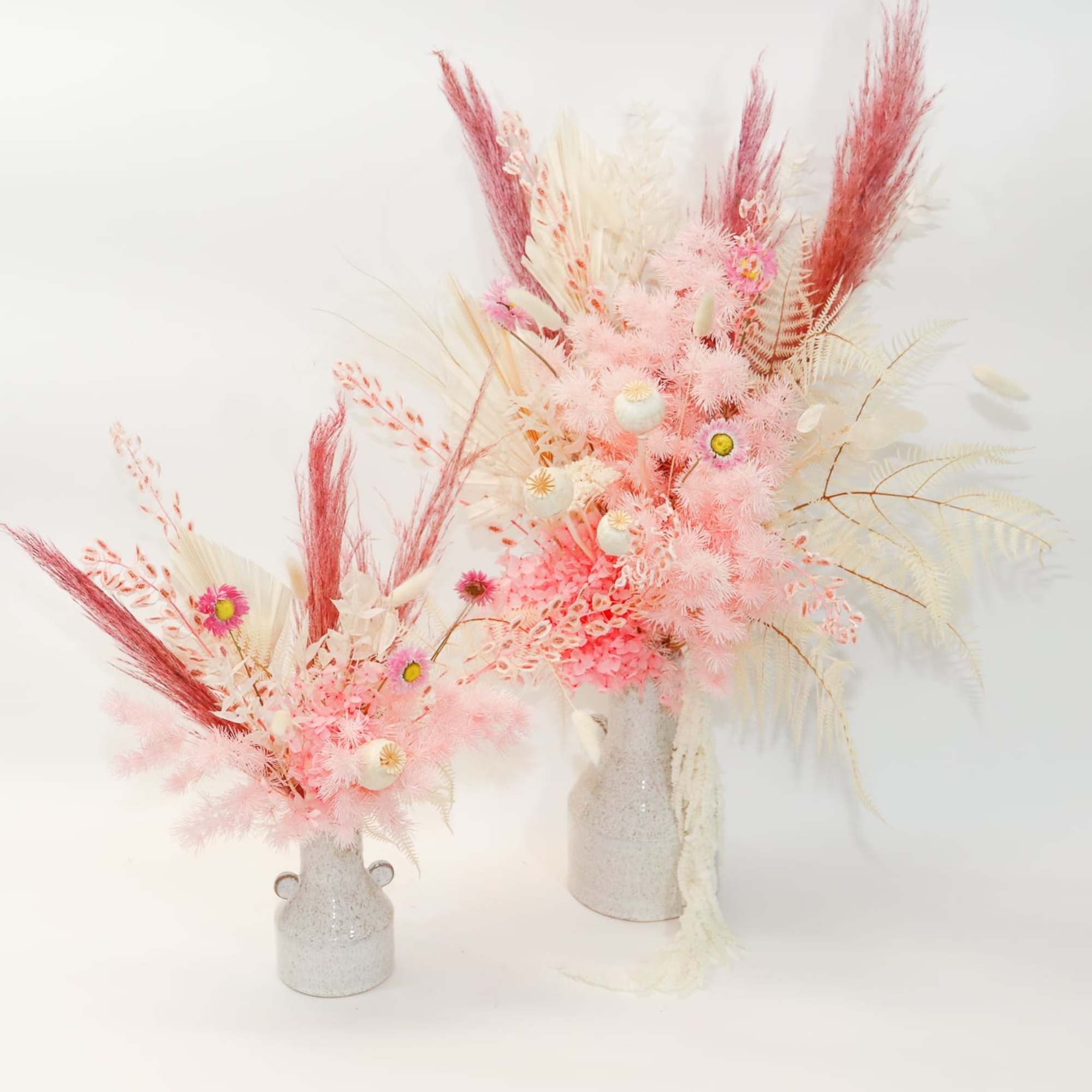 Two pink and white dried floral arrangements in small vases
