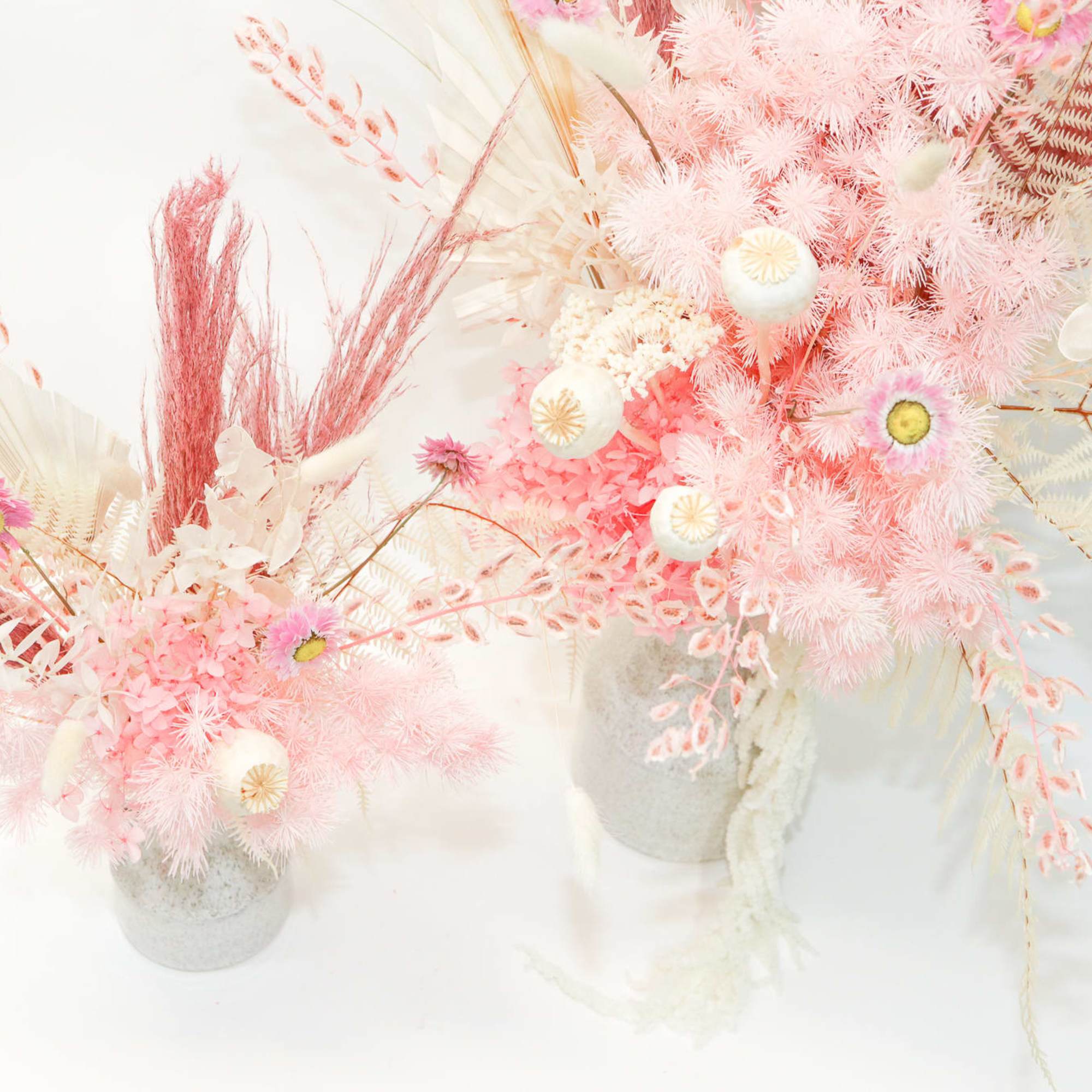 Two pastel pink floral arrangements in white vases with airy dried accents