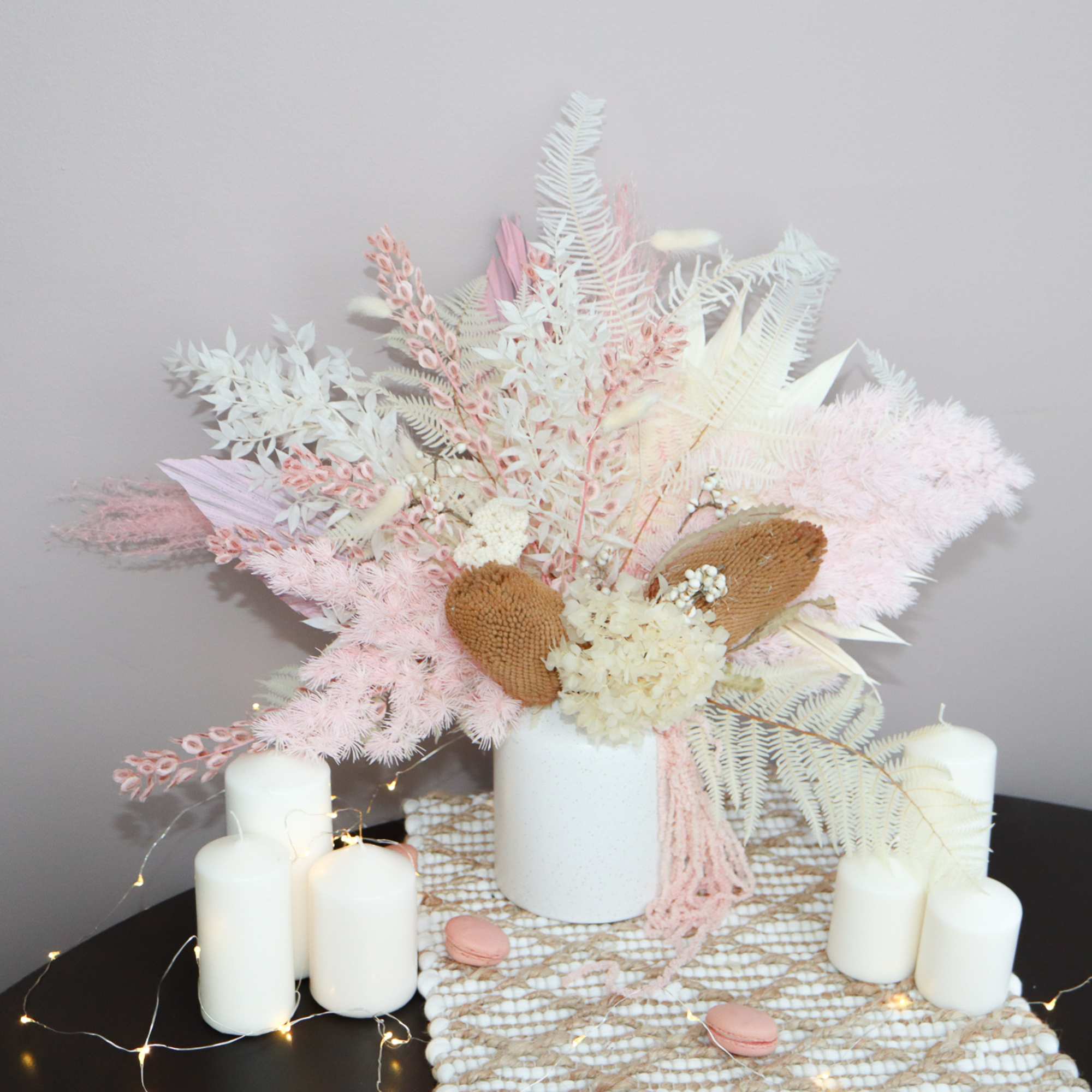 Pastel dried floral arrangement in a white vase with candles on a table