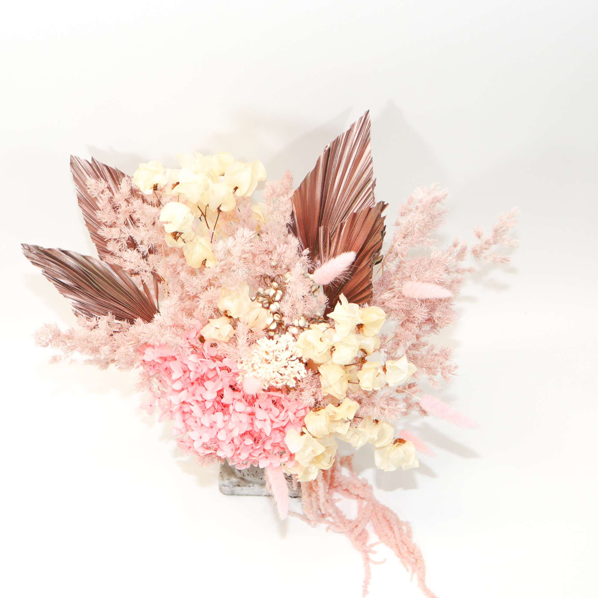 Pink and cream floral arrangement with dried palm leaves in a small vase