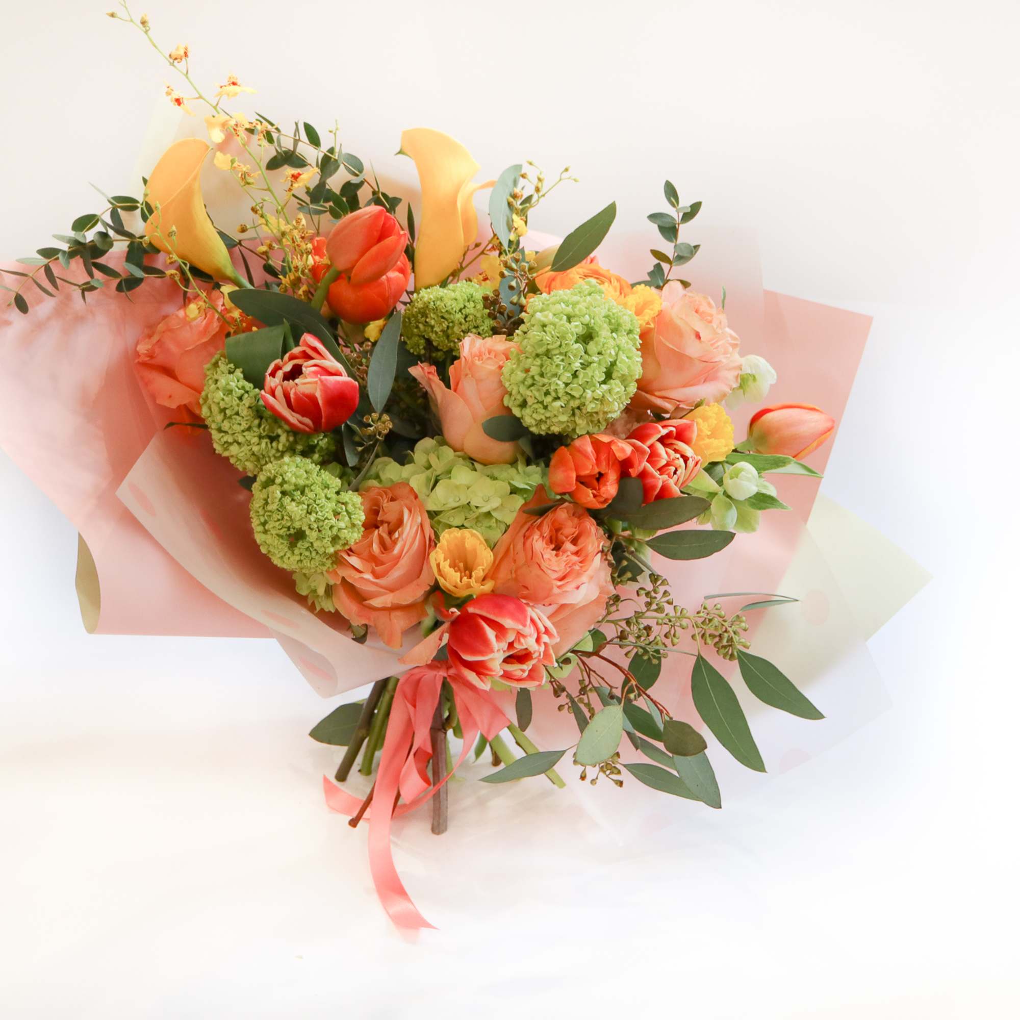 Bouquet of peach, coral, and yellow flowers wrapped in pink paper