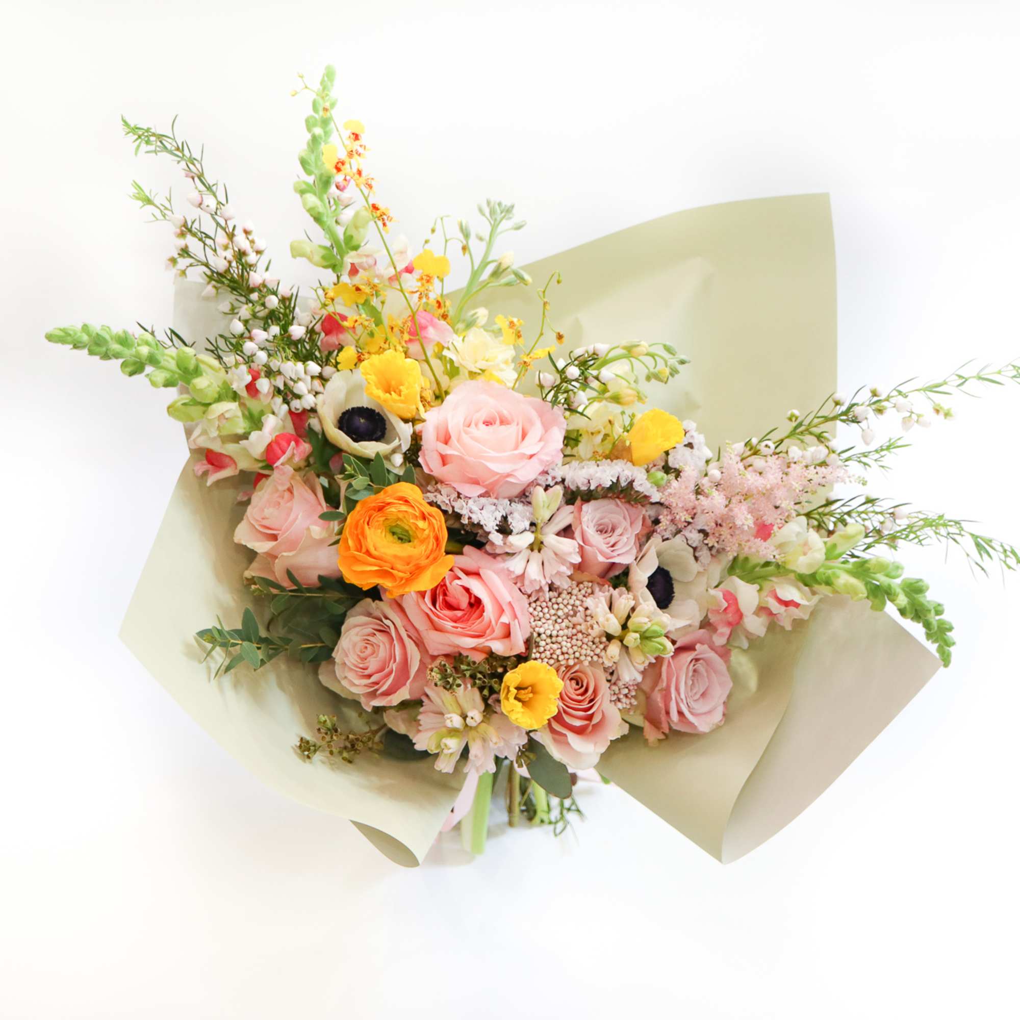 Mixed bouquet of pink, yellow, and white flowers wrapped in pale paper