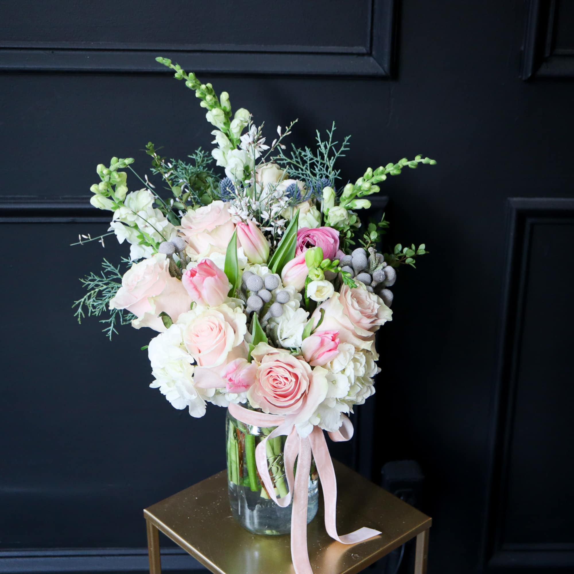 Pink and white floral arrangement in a glass vase with a pink ribbon