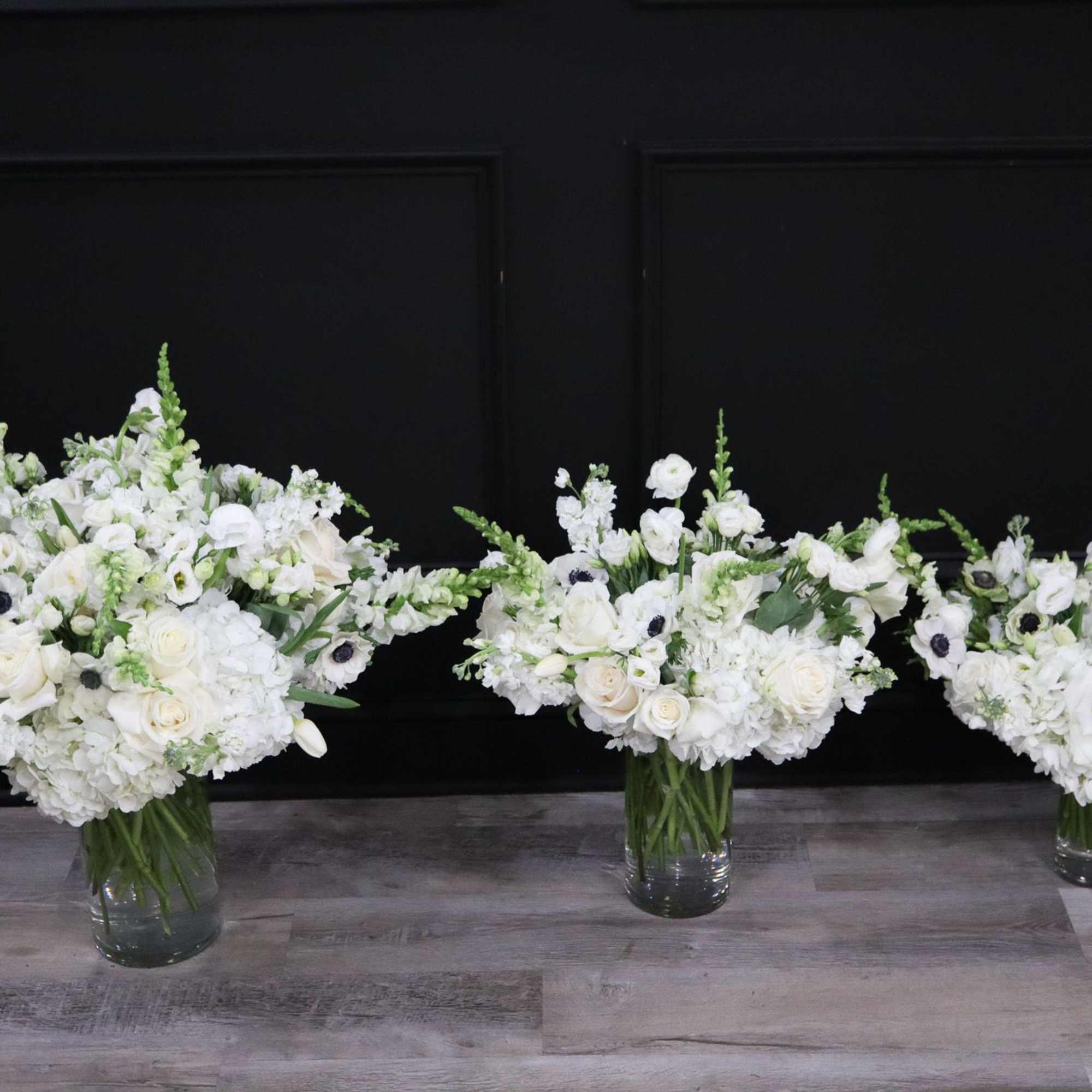 Three white floral arrangements in clear glass vases