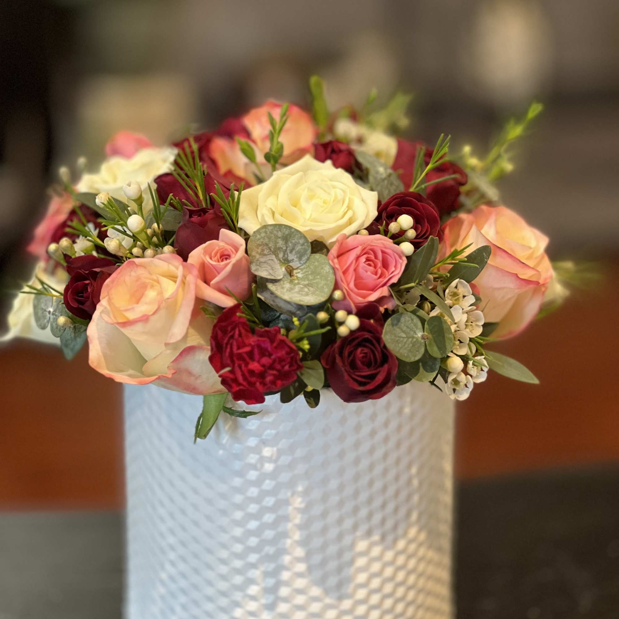 Mixed roses in pink, cream, and burgundy arranged in a white vase