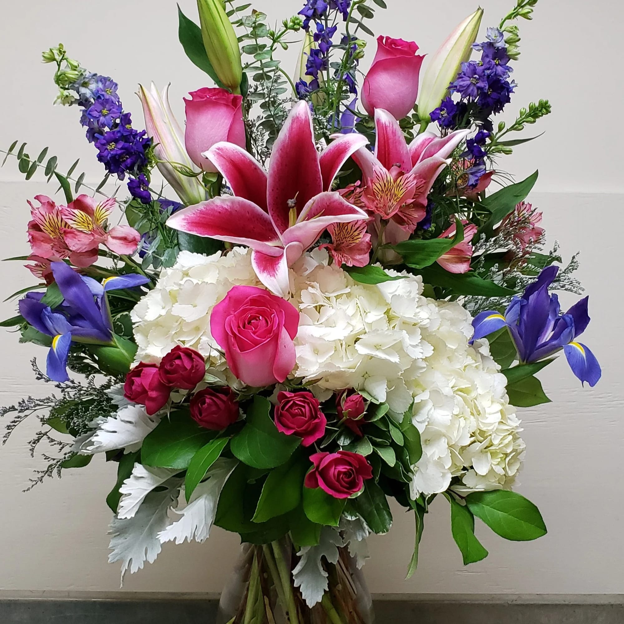 Mixed bouquet with pink lilies, roses, hydrangeas, and purple irises in a glass vase