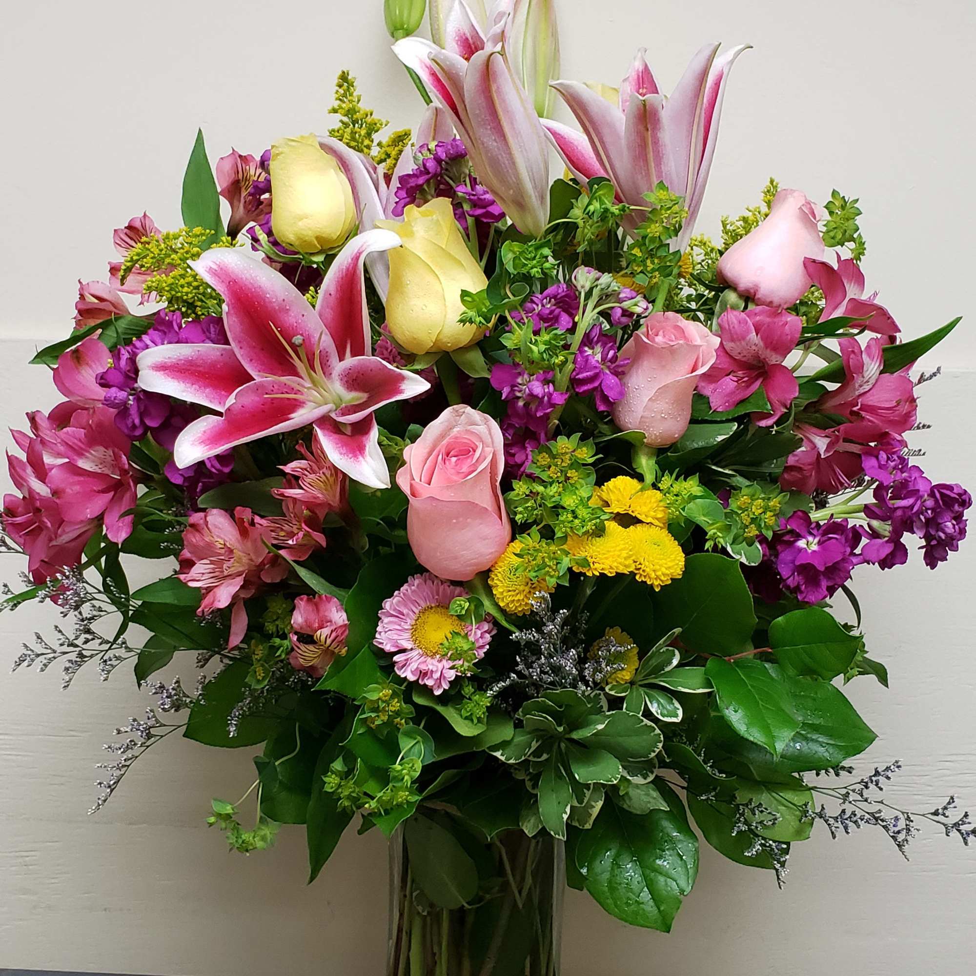 Large mixed bouquet of pink lilies, roses, and yellow flowers in a glass vase