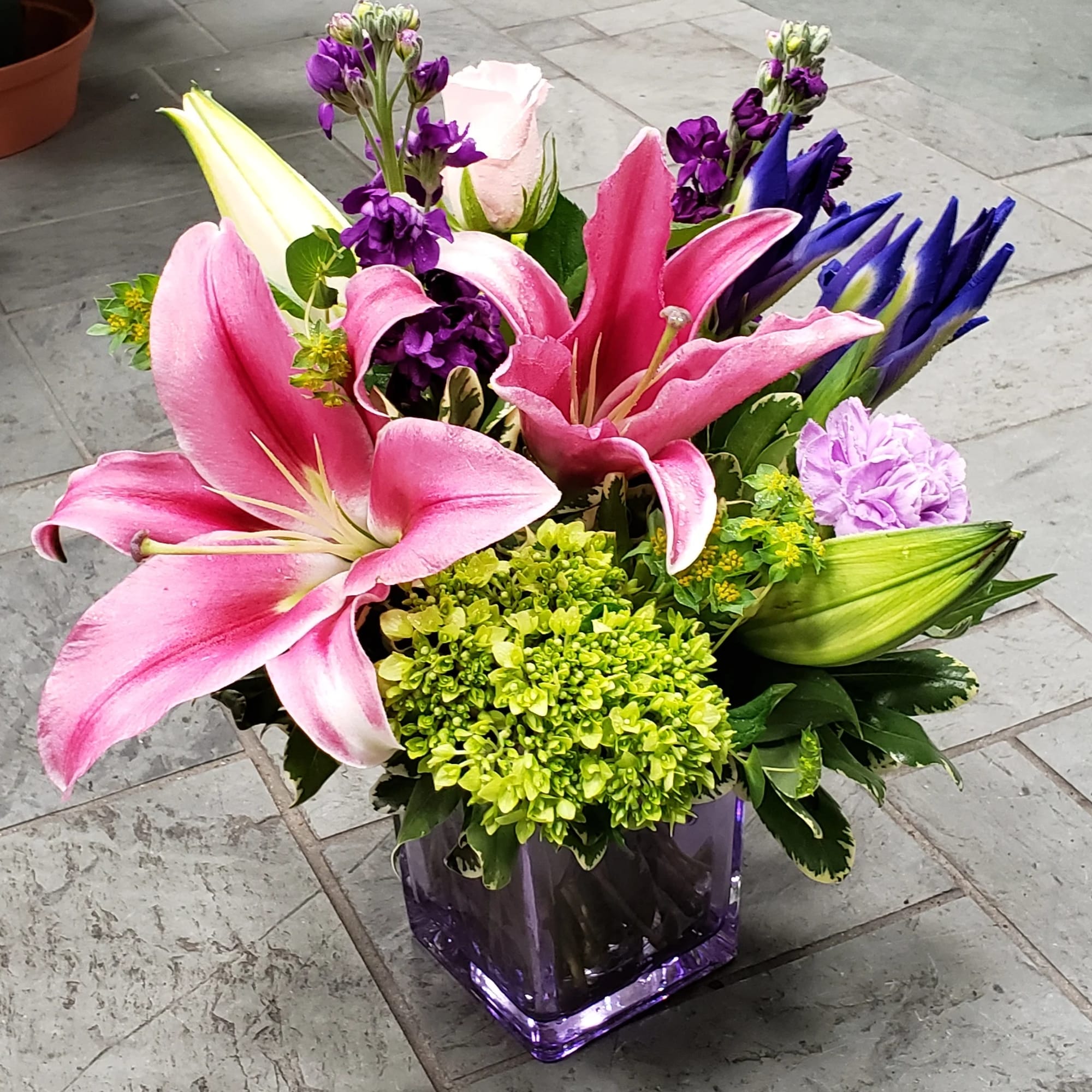 Pink lilies and purple flowers arranged in a purple glass vase
