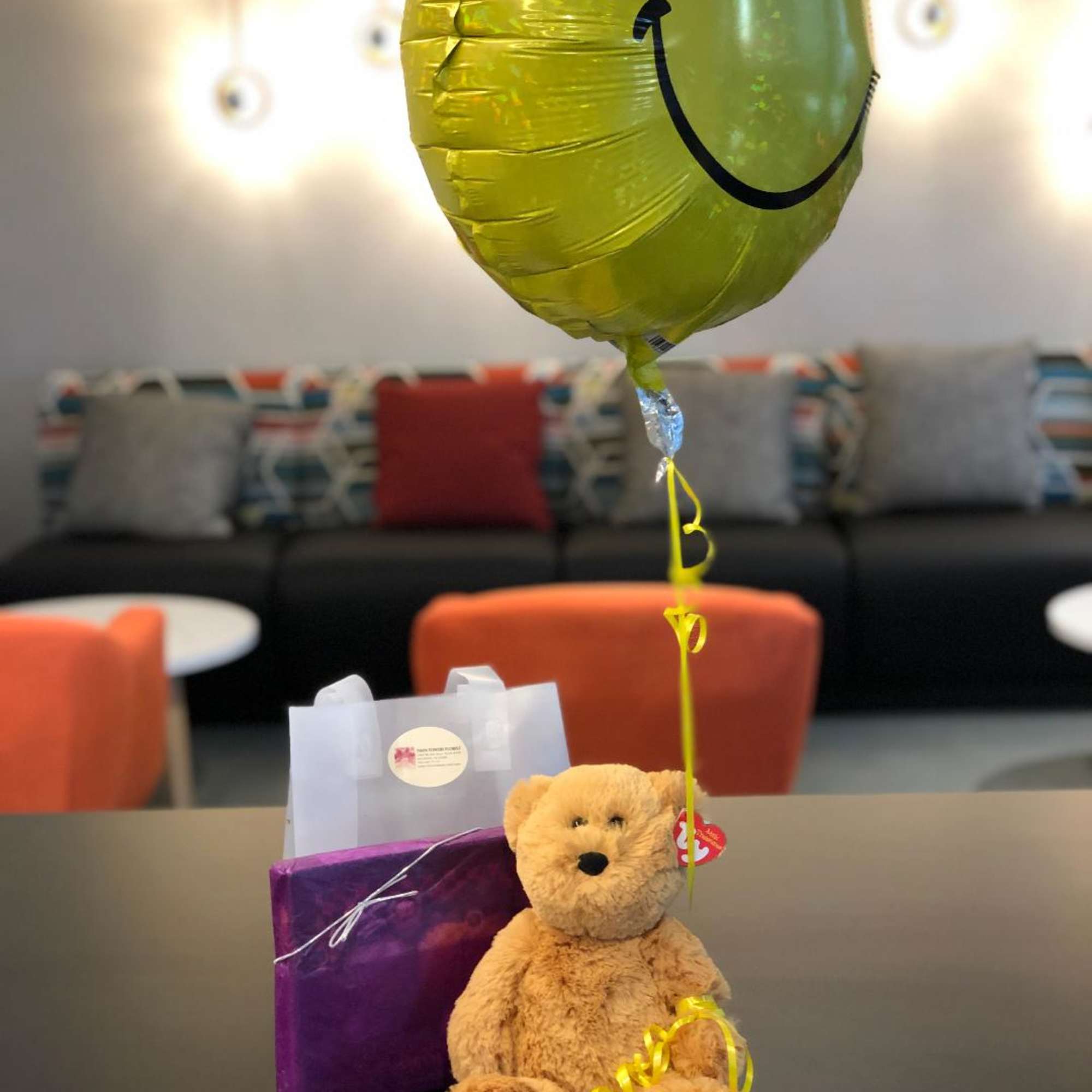 Yellow smiley-face balloon with a teddy bear and gift bags on a table