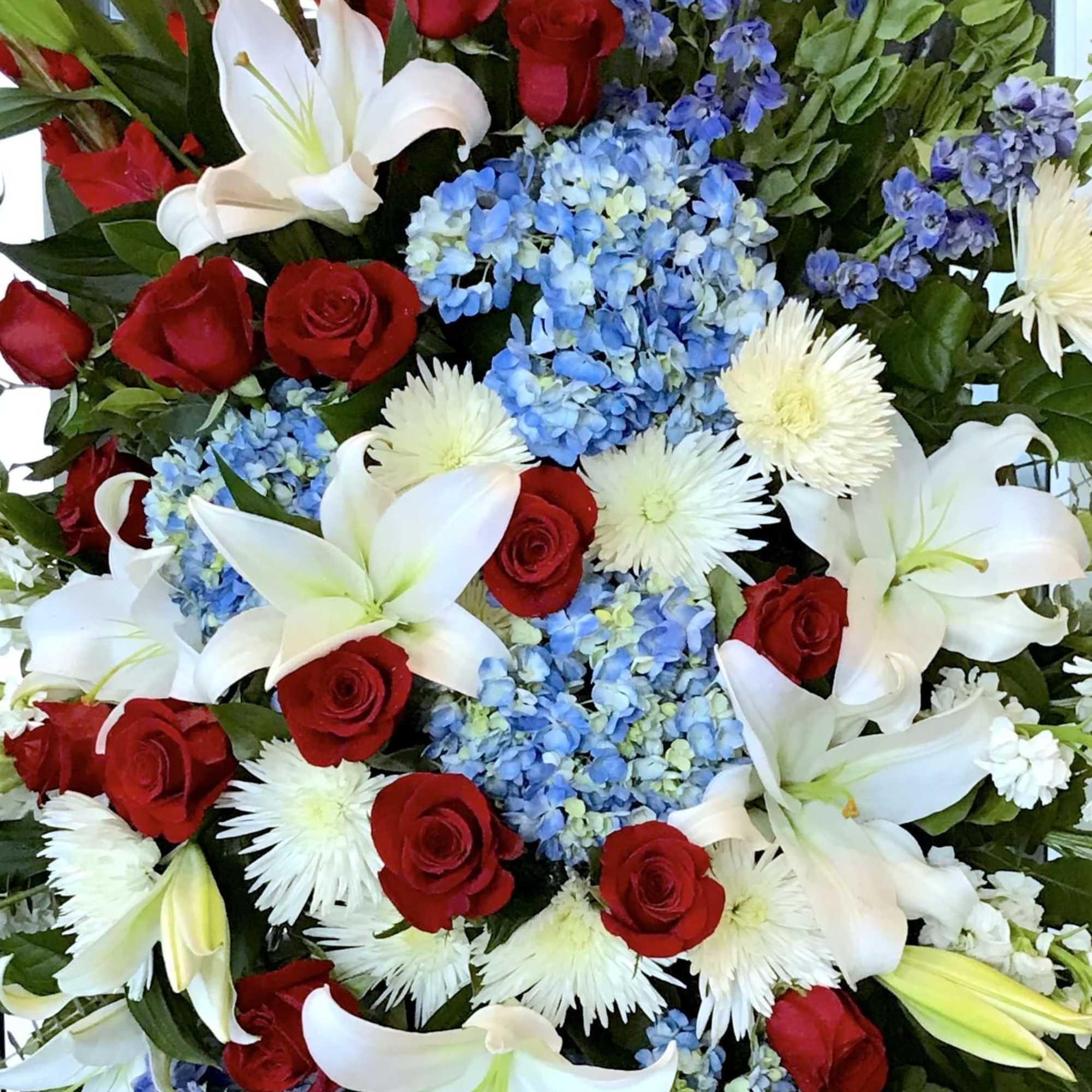 Tall arrangement of red roses, white lilies, and blue hydrangeas with delphinium