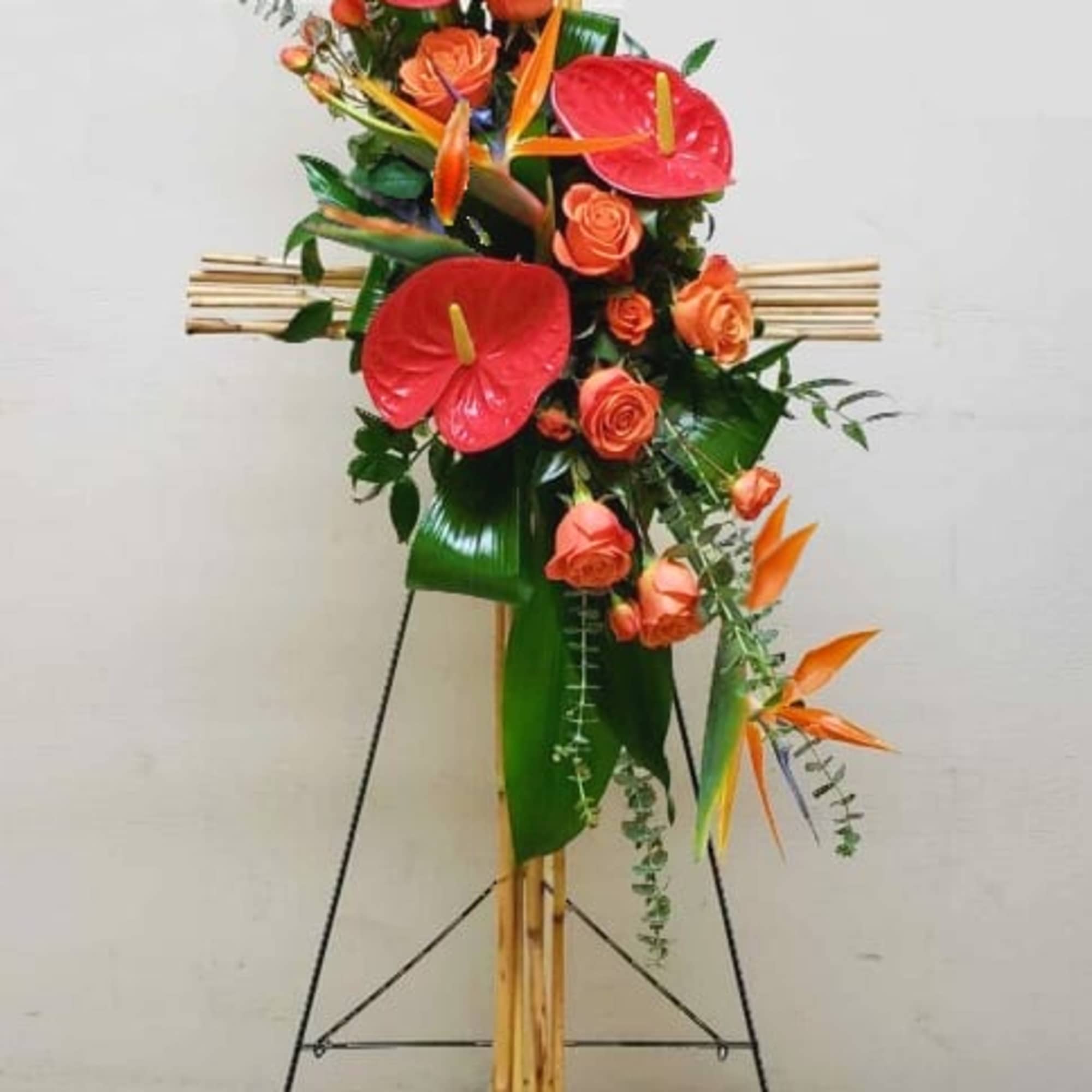 Tall bamboo cross spray with orange roses, red tropical blooms, and birds of paradise on a stand