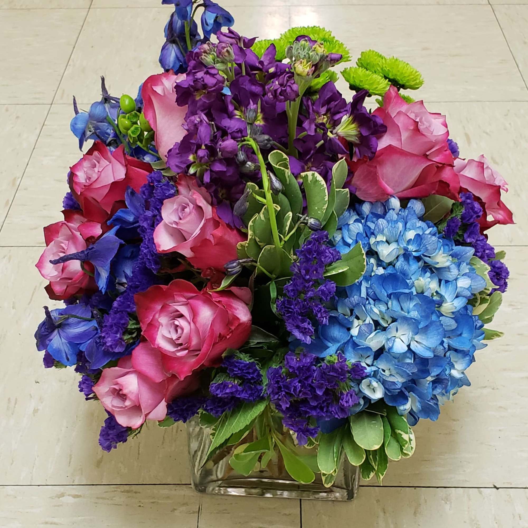 Bouquet of pink roses, blue hydrangeas, and purple flowers in a glass vase