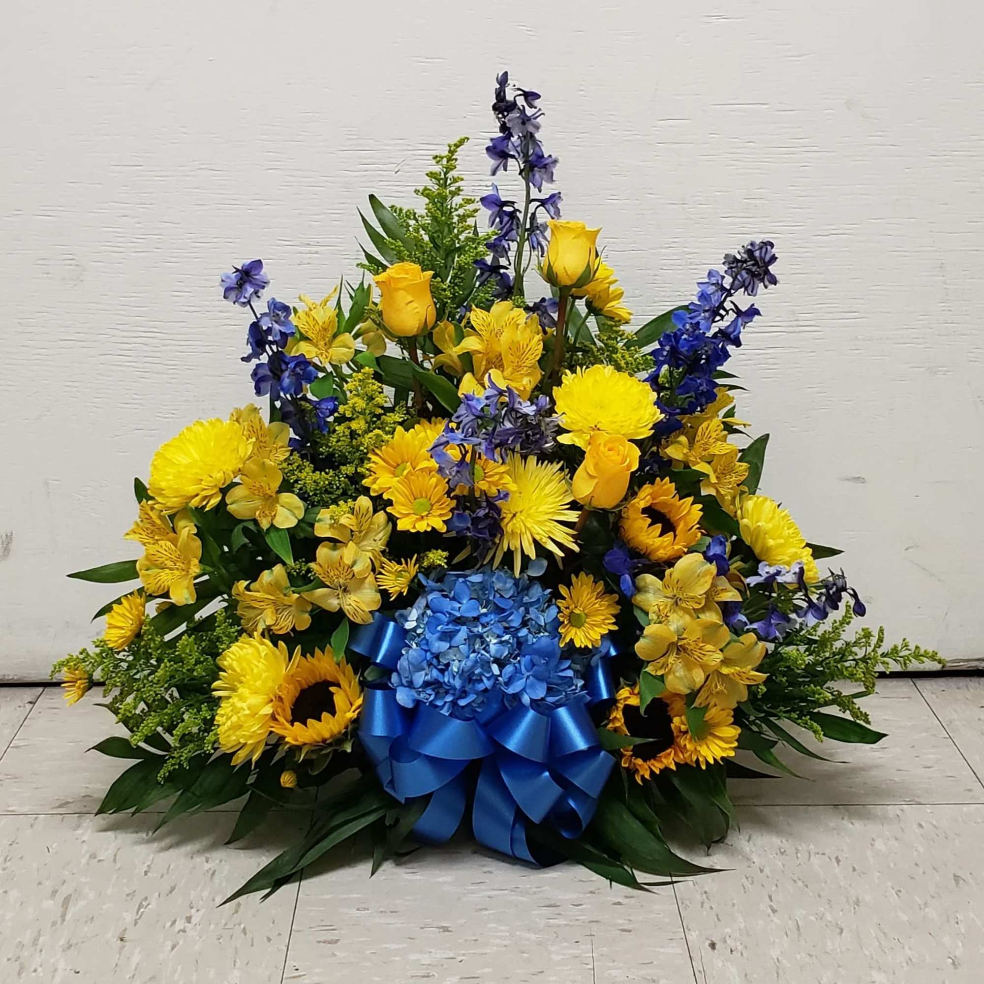 Fan-shaped yellow and blue flower arrangement with a large blue ribbon at the base