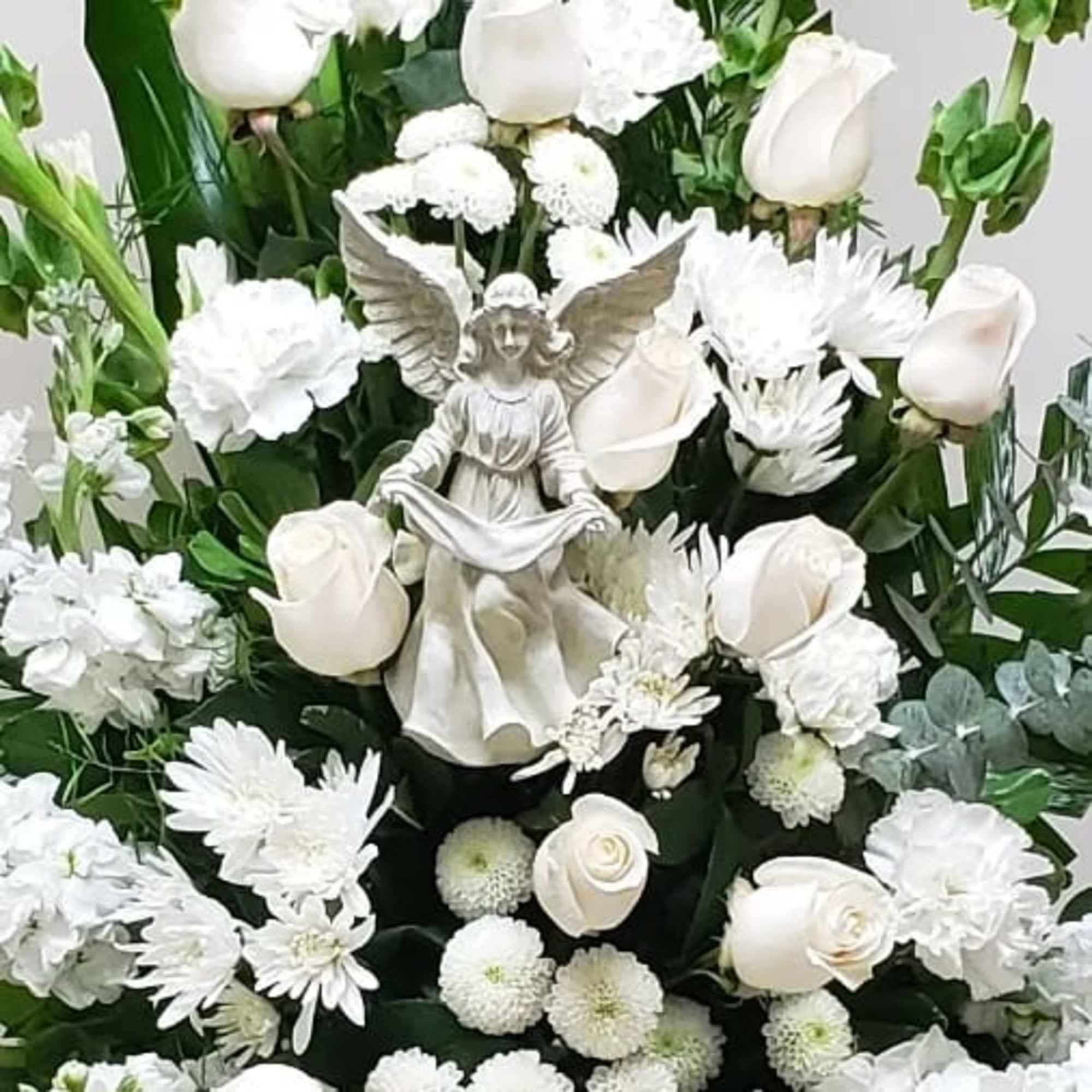 Tall white floral arrangement with roses, carnations, and mums surrounding a central angel figurine