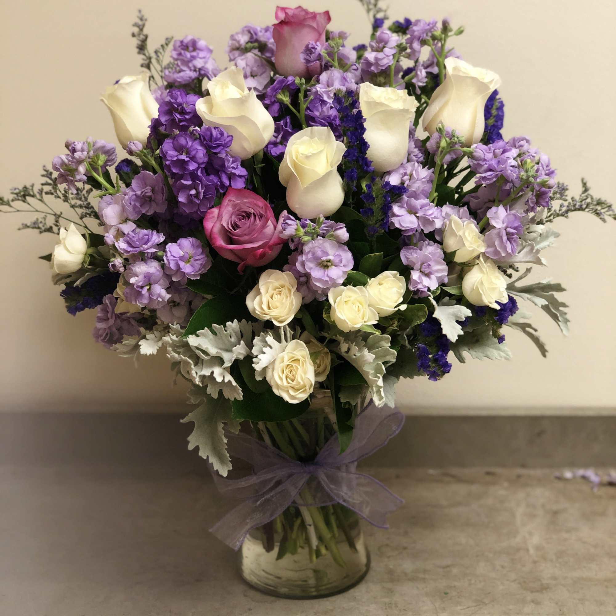 Bouquet of purple and white roses in a glass vase with a lavender ribbon