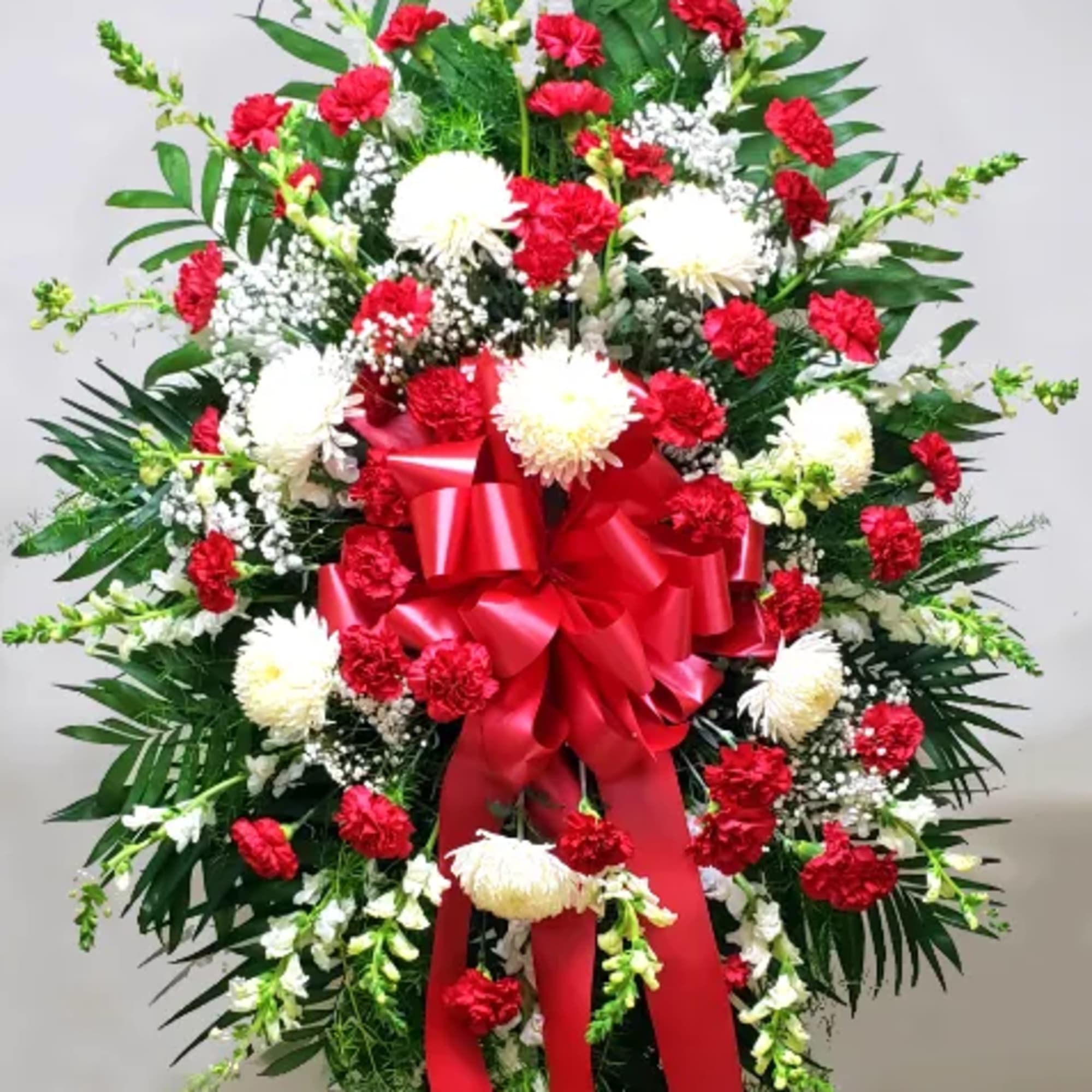 Tall standing spray of red carnations and white flowers with greenery and a large red bow on an easel