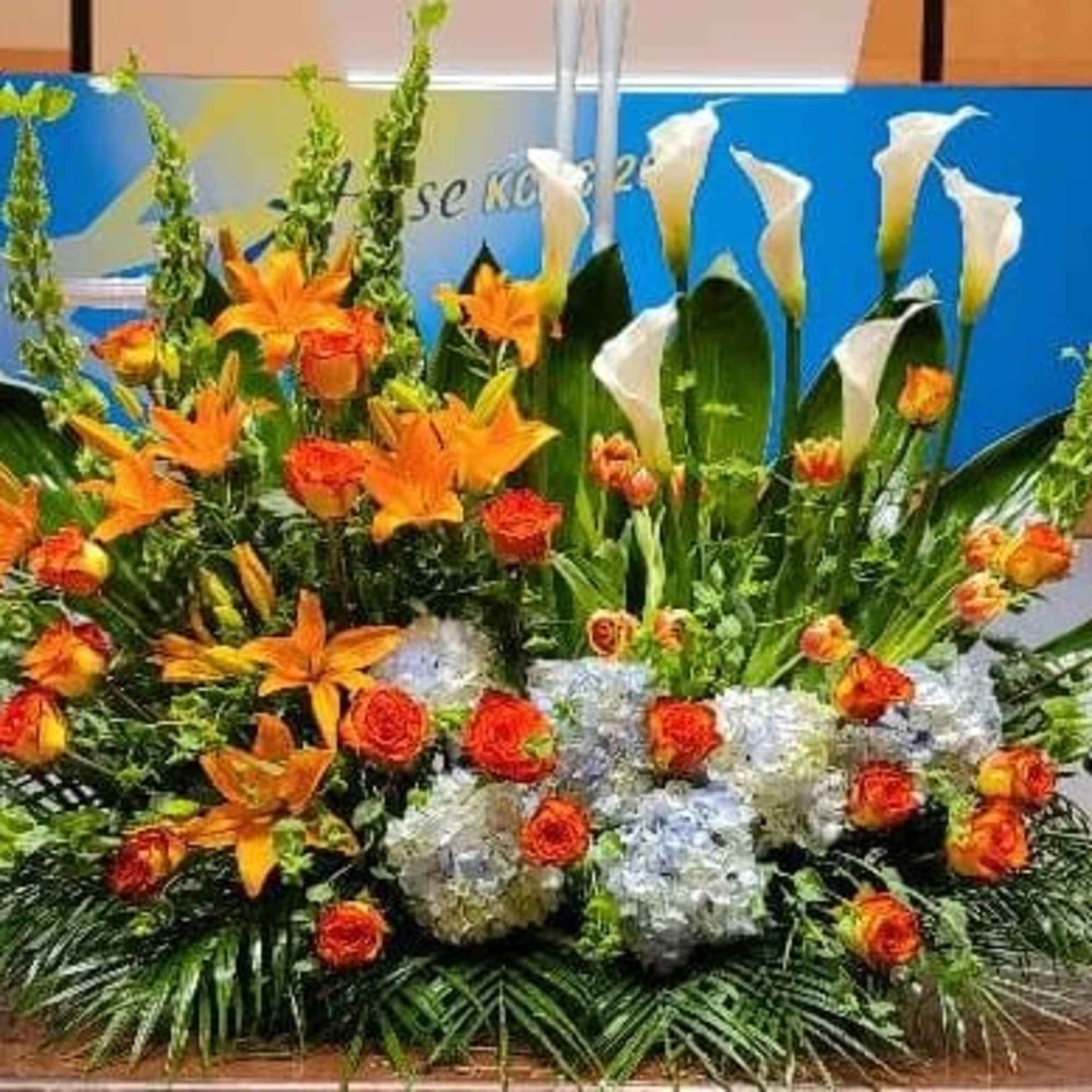 Large stage floral arrangement with orange lilies, orange roses, white calla lilies, and white hydrangeas.