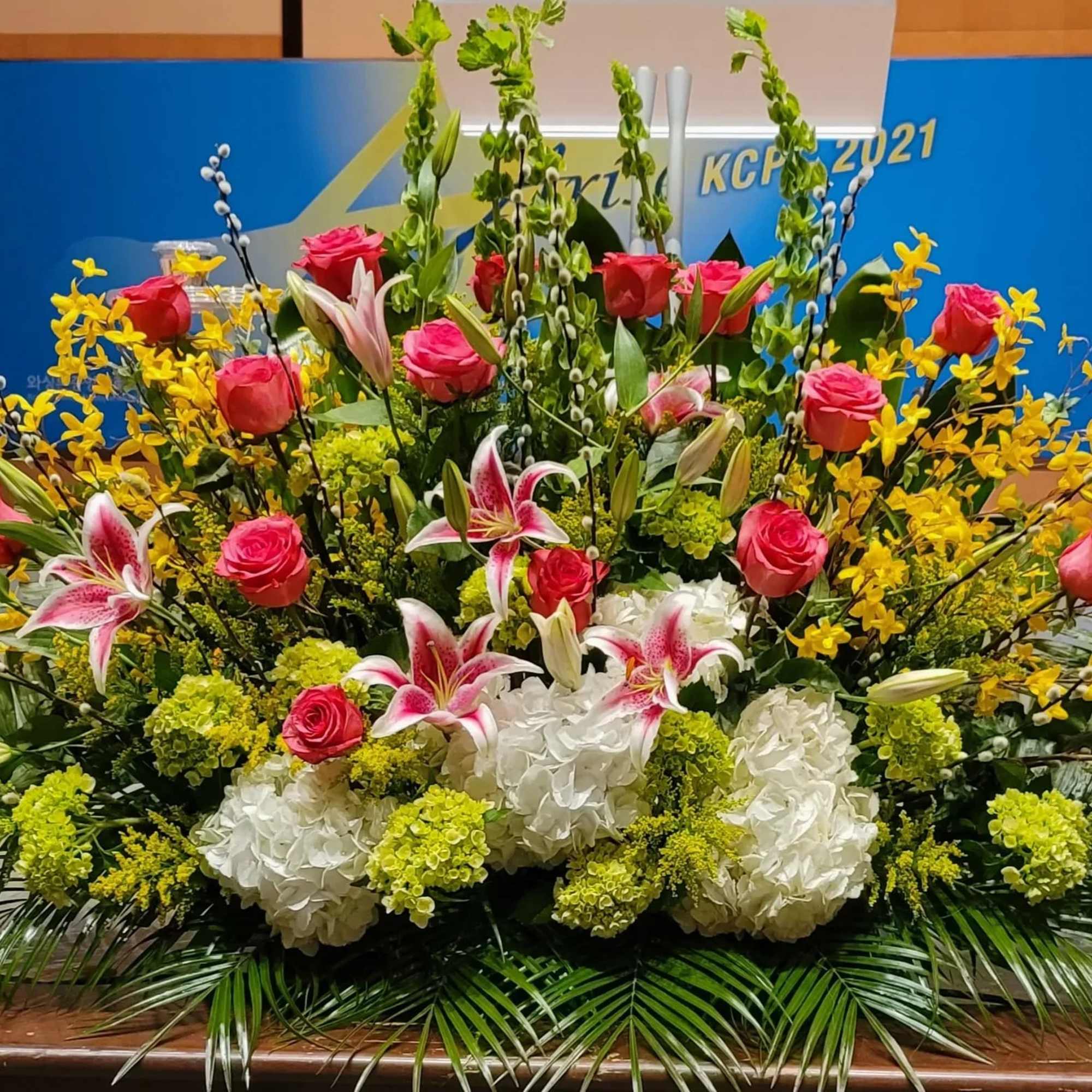 Large stage floral arrangement with pink roses, stargazer lilies, white hydrangeas and yellow flowers