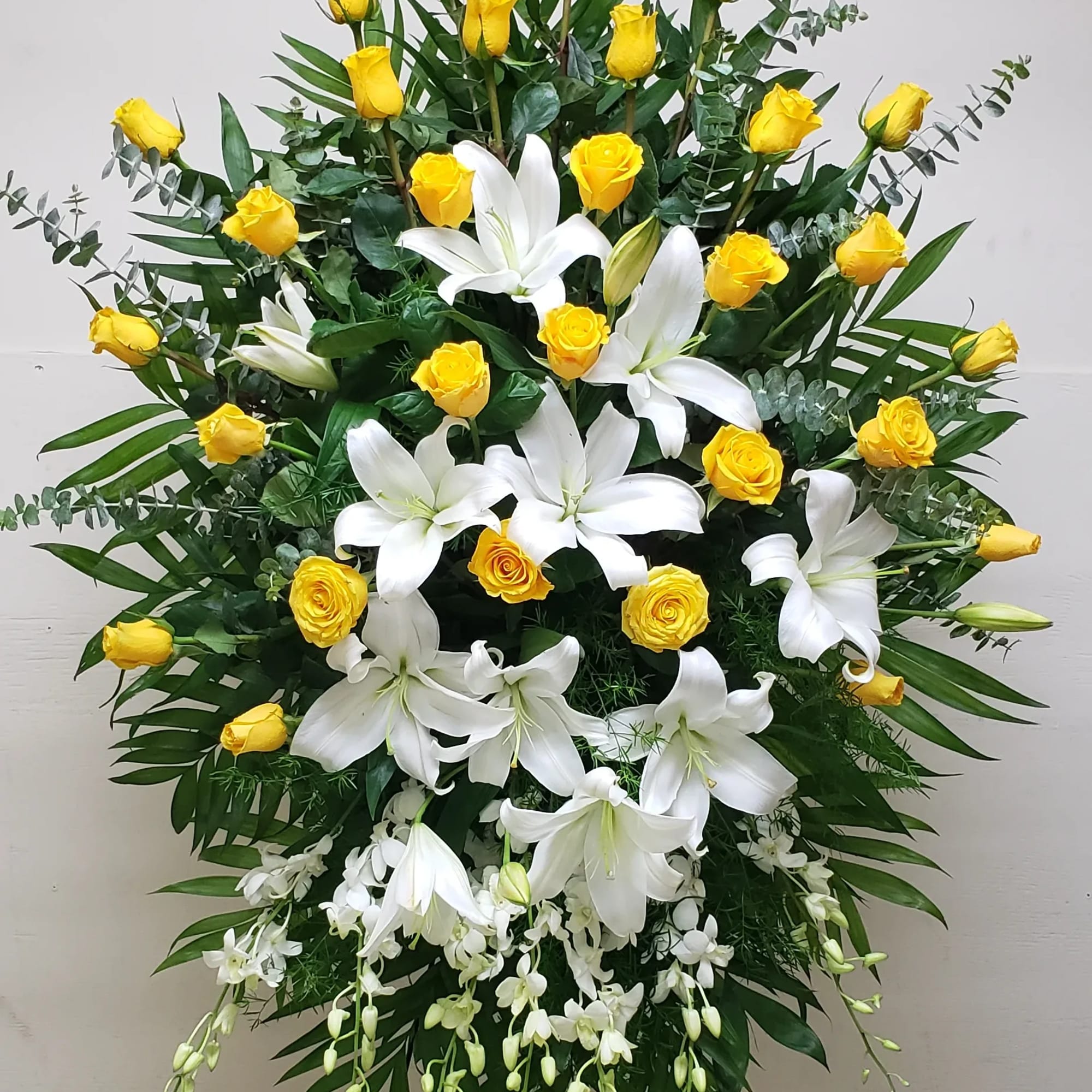 Tall standing spray of yellow roses and white lilies with cascading white orchids on a metal easel