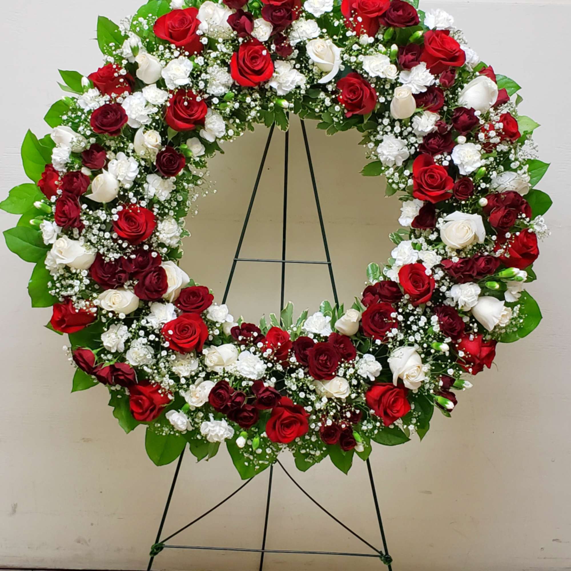 Large standing wreath of red and white roses with white accent flowers on a metal easel.