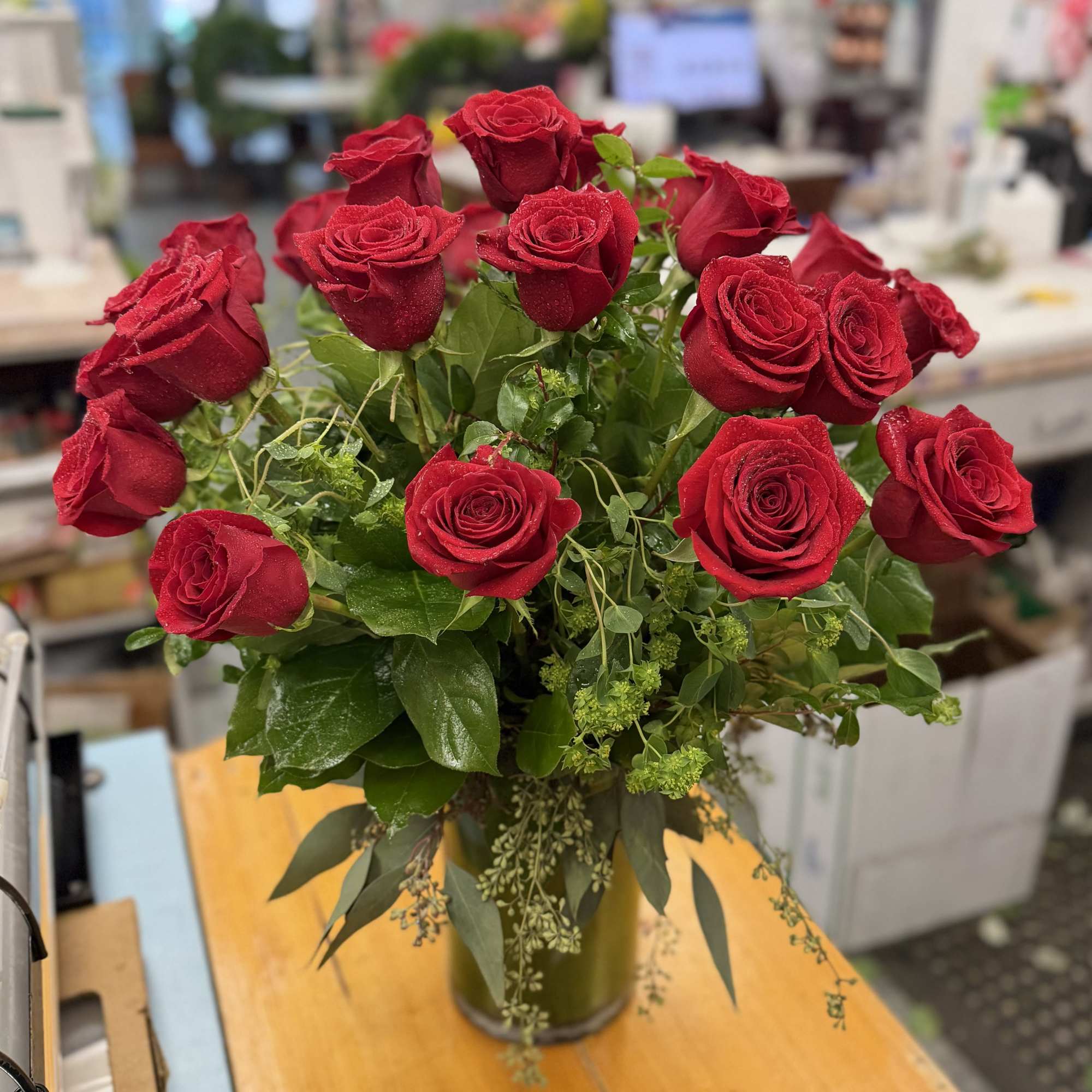Red roses arranged in a glass vase with mixed greenery
