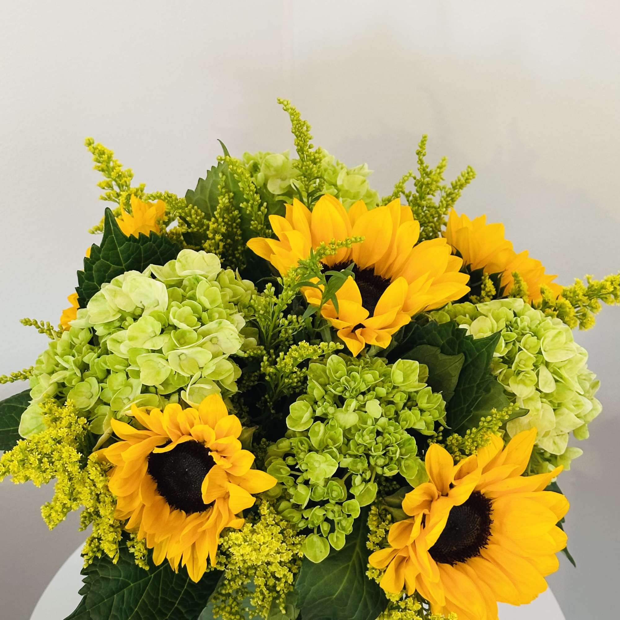 Sunflowers and green hydrangeas arranged in a square glass vase