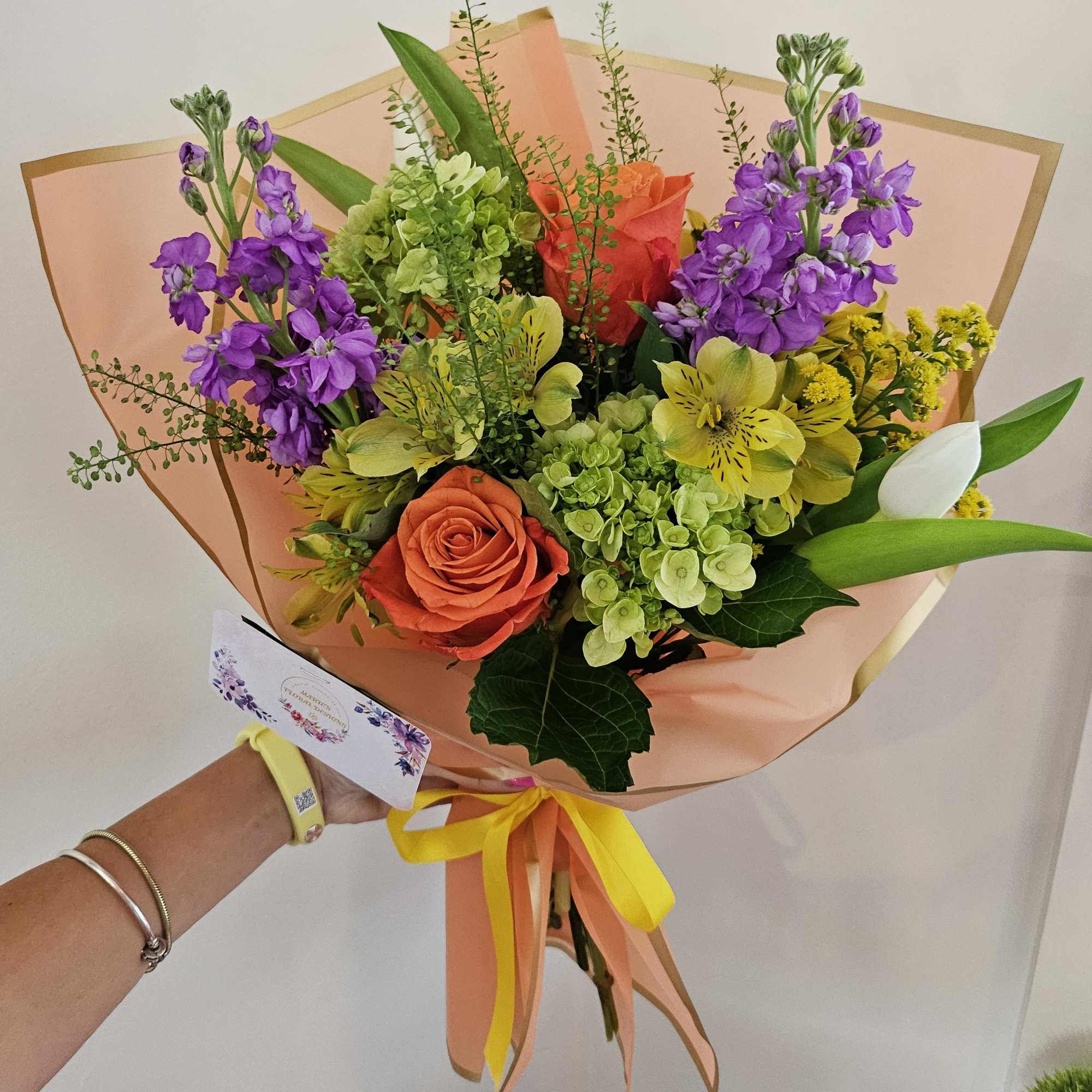 Bouquet of orange roses, purple flowers, and green hydrangeas in peach wrap