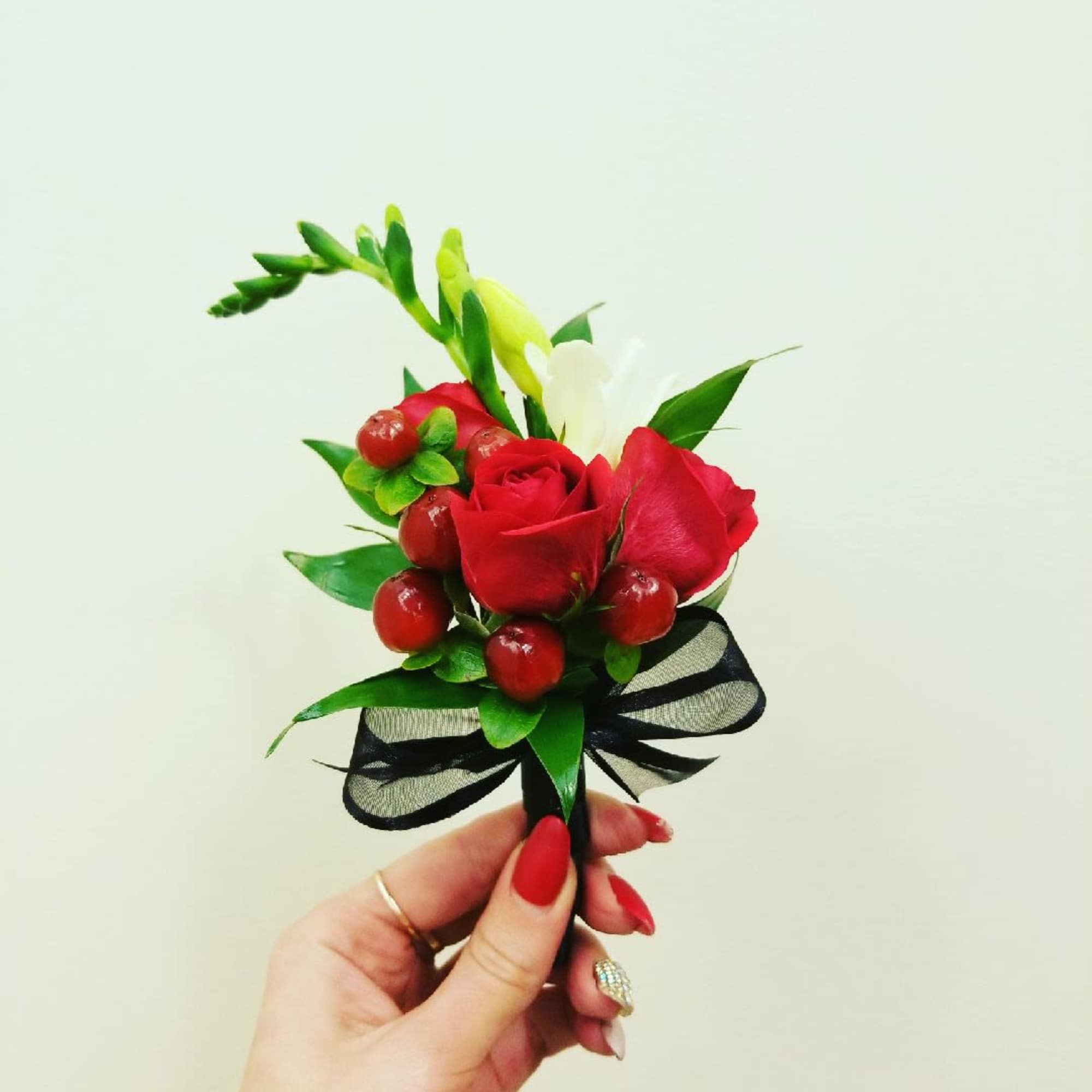 Small red rose boutonniere with berries and a black ribbon bow