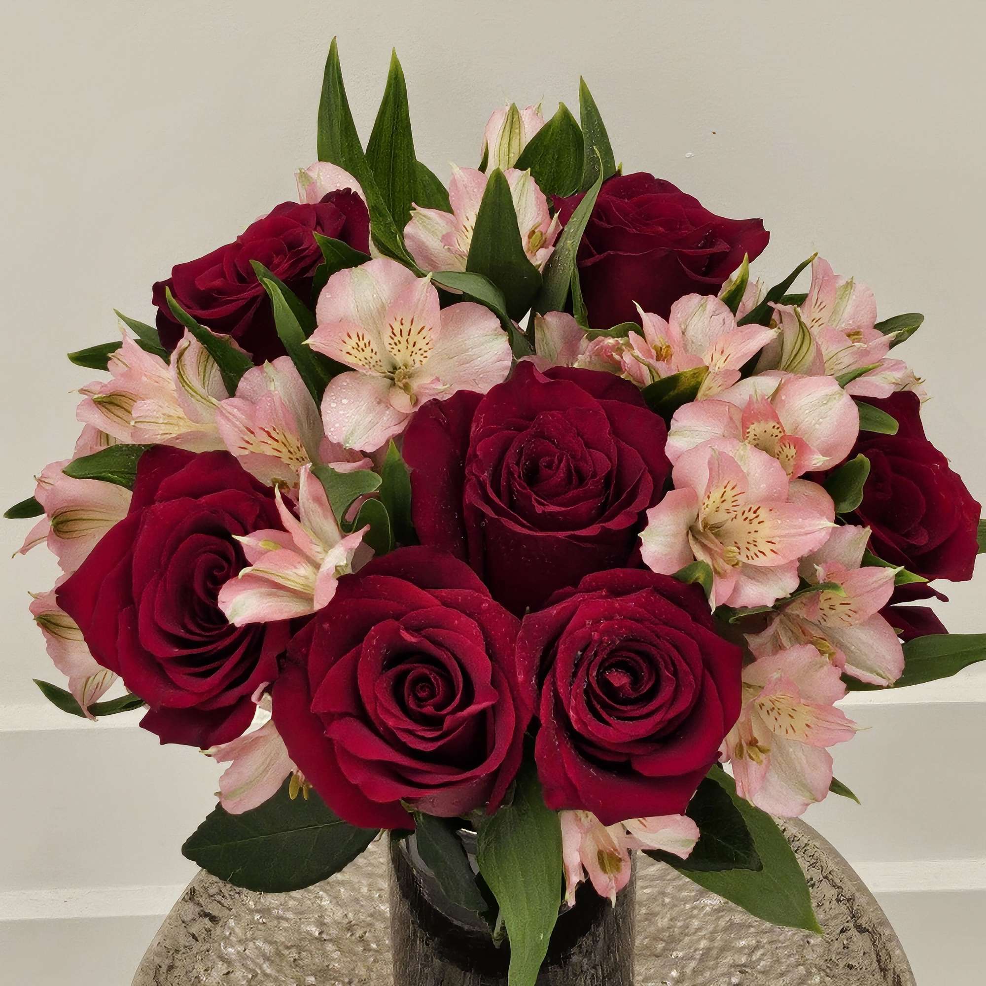 Red roses and pink alstroemeria in a dark glass vase