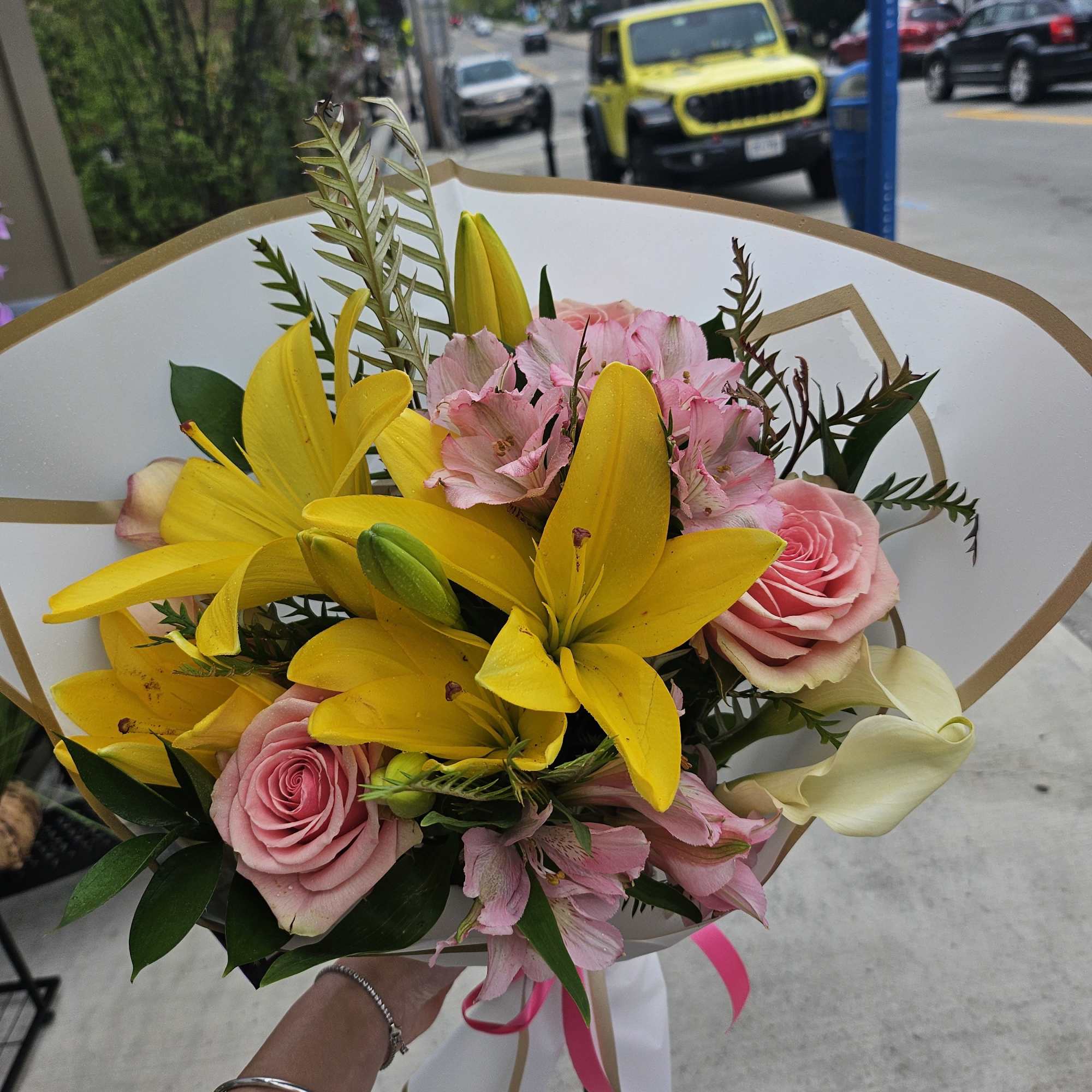Bouquet of yellow lilies, pink roses, and pale pink flowers wrapped in white paper