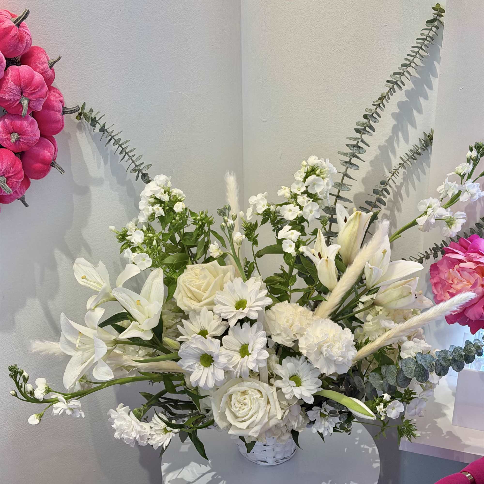 White floral arrangement in a low vase with lilies, roses, and daisies