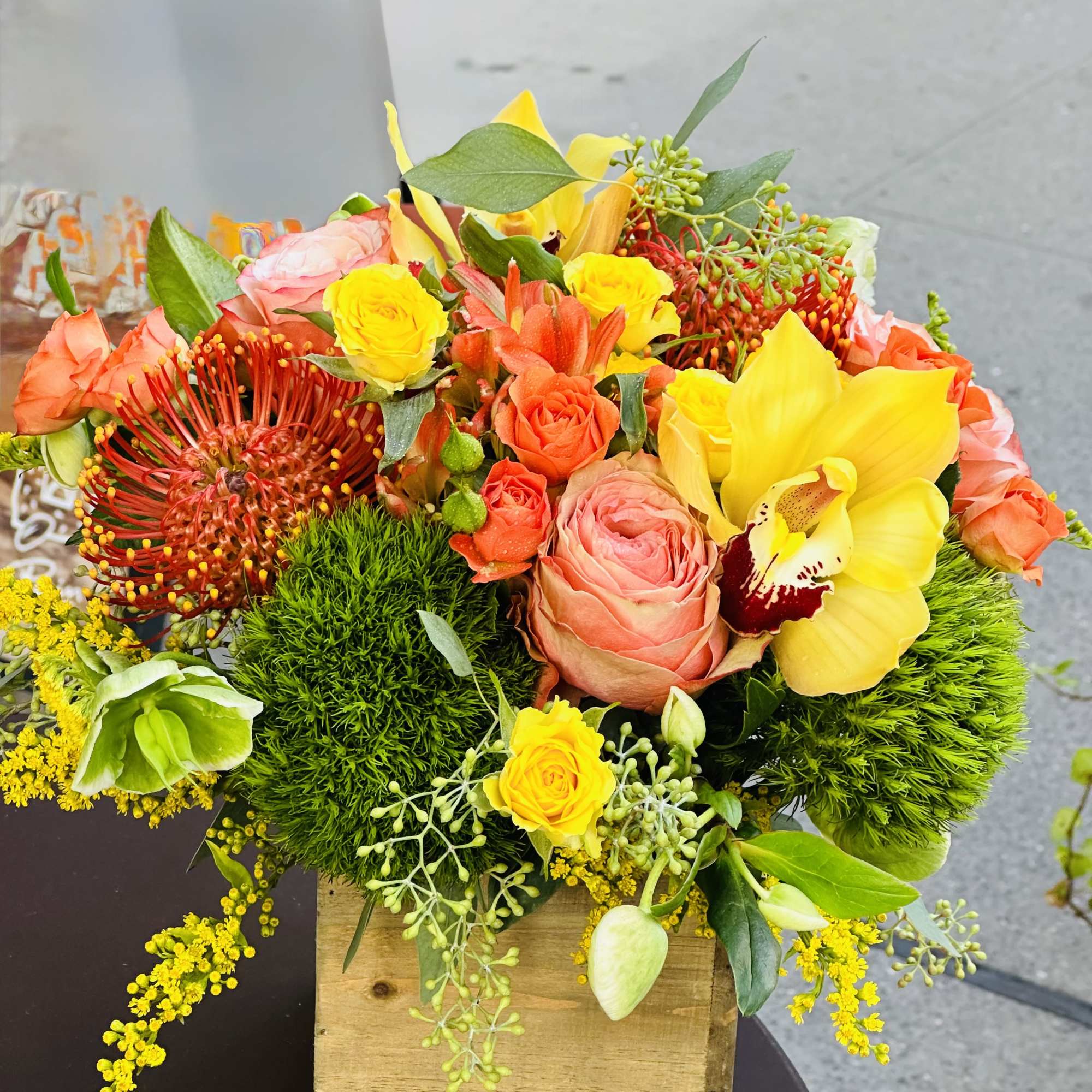 Bright mixed bouquet in a wooden box with yellow, orange, and pink blooms