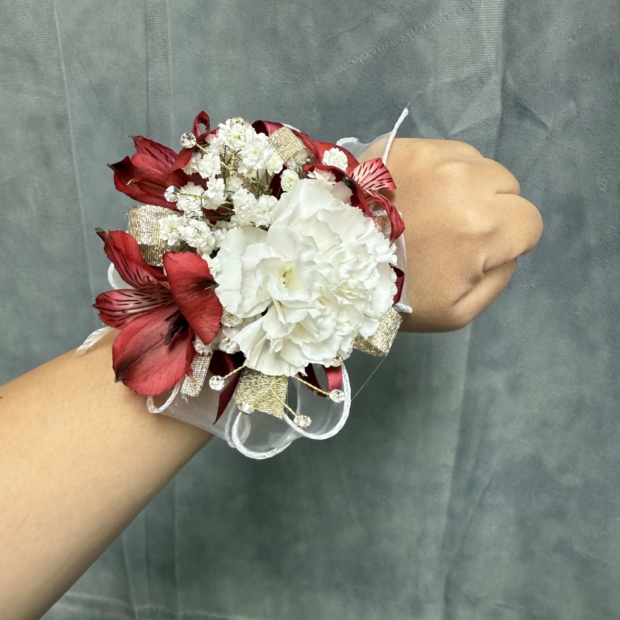 White carnation wrist corsage with red alstroemeria accents, gold accents , rhinestones